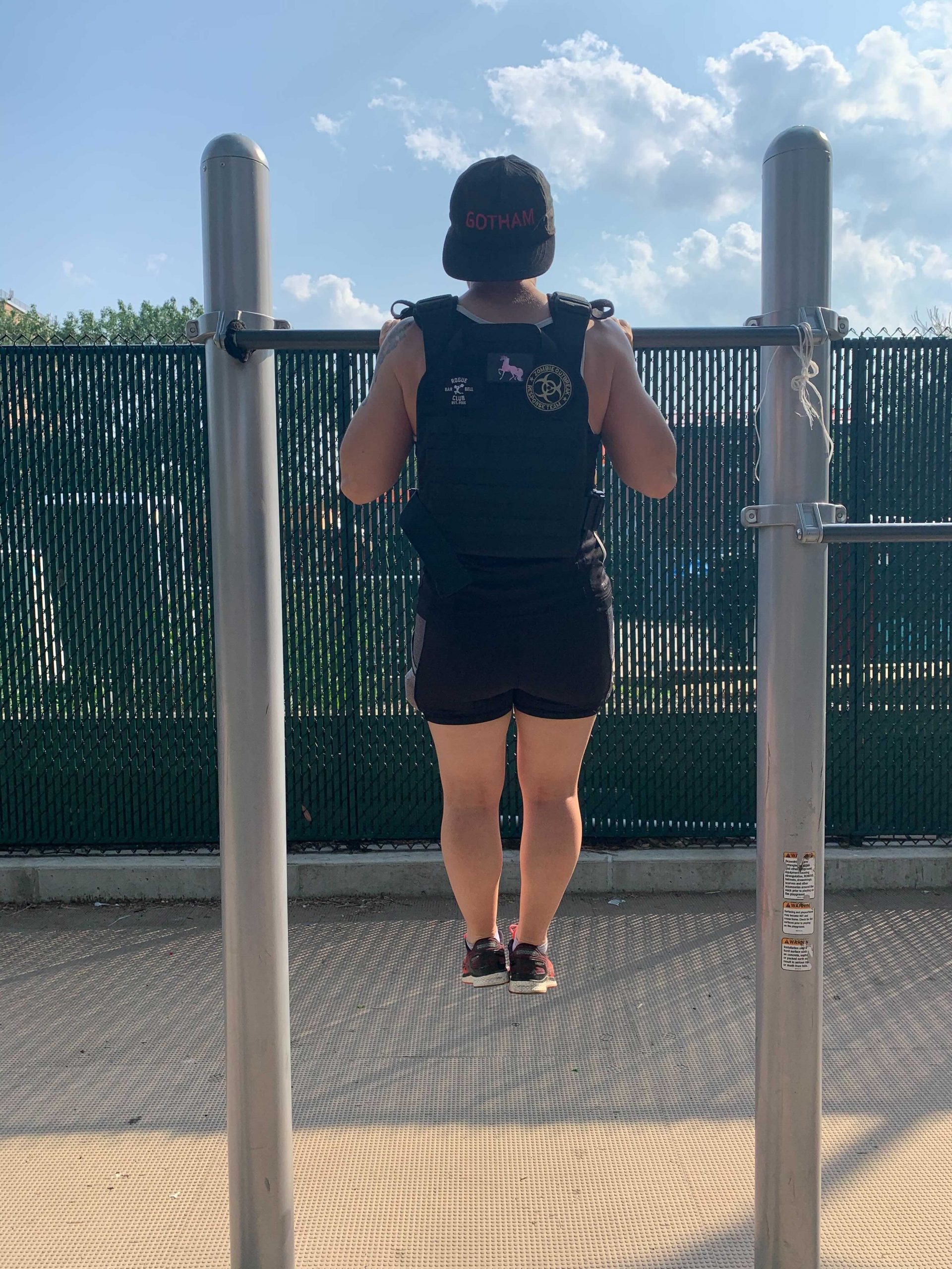 a sweaty fitness reporter at the top of a pull-up on a playground, wearing a weight vest