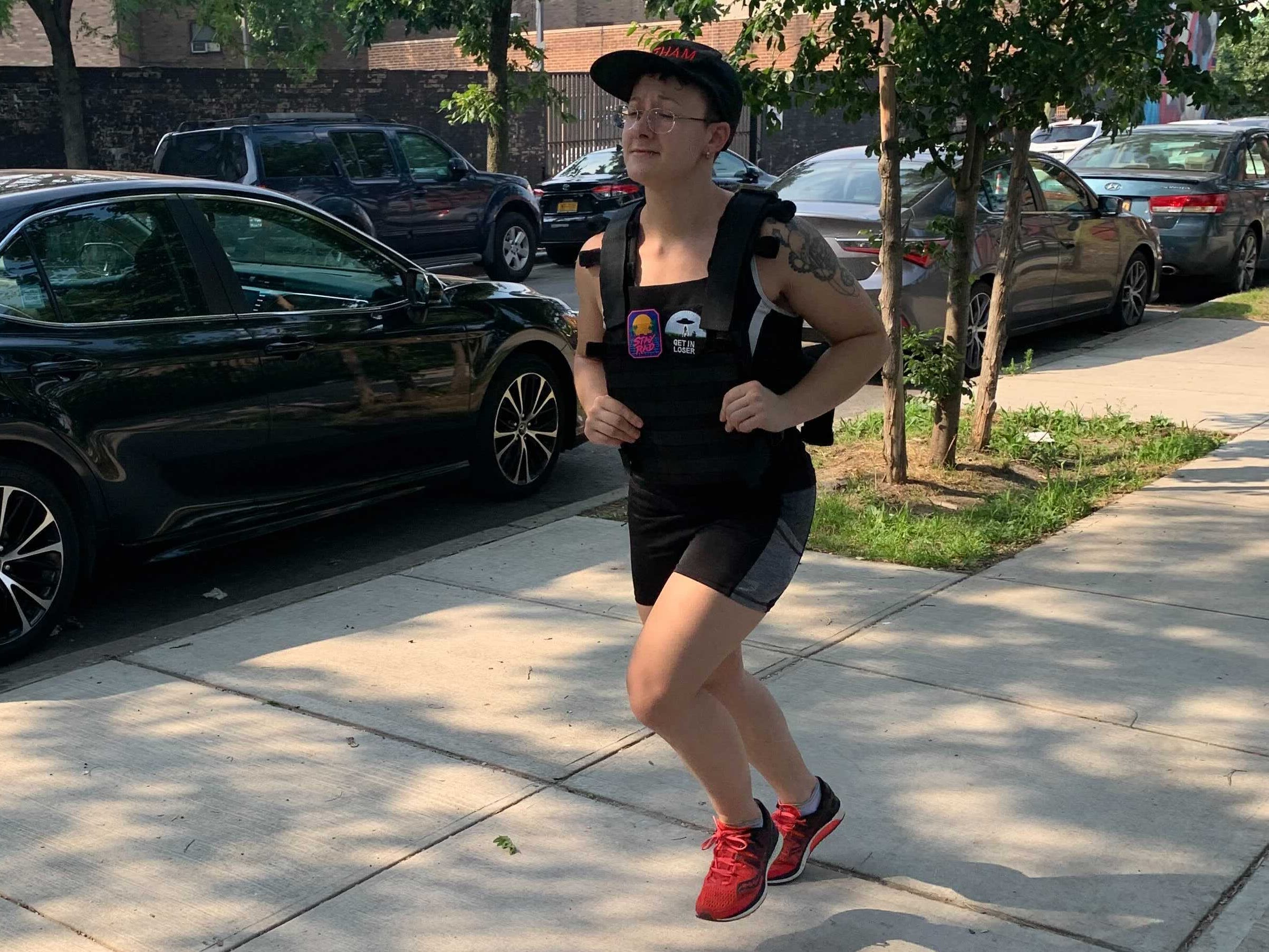 a fitness reporter running with a weight vest down a shaded street in the sunshine, sweating profusely