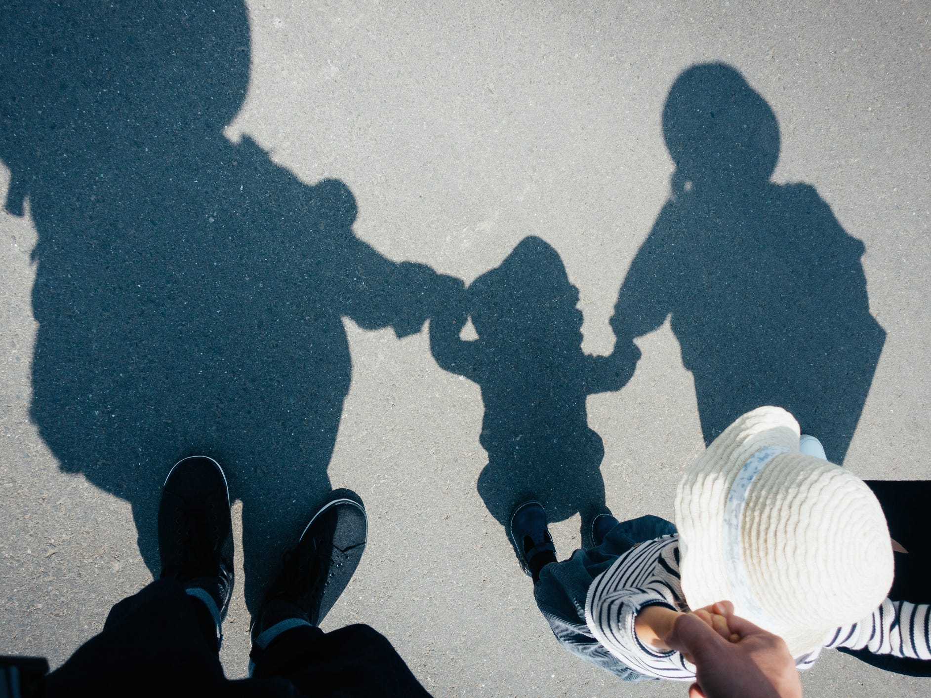 Shadow on gravel path of a loving family of three holding hands walking outdoors on a lovely sunny day.