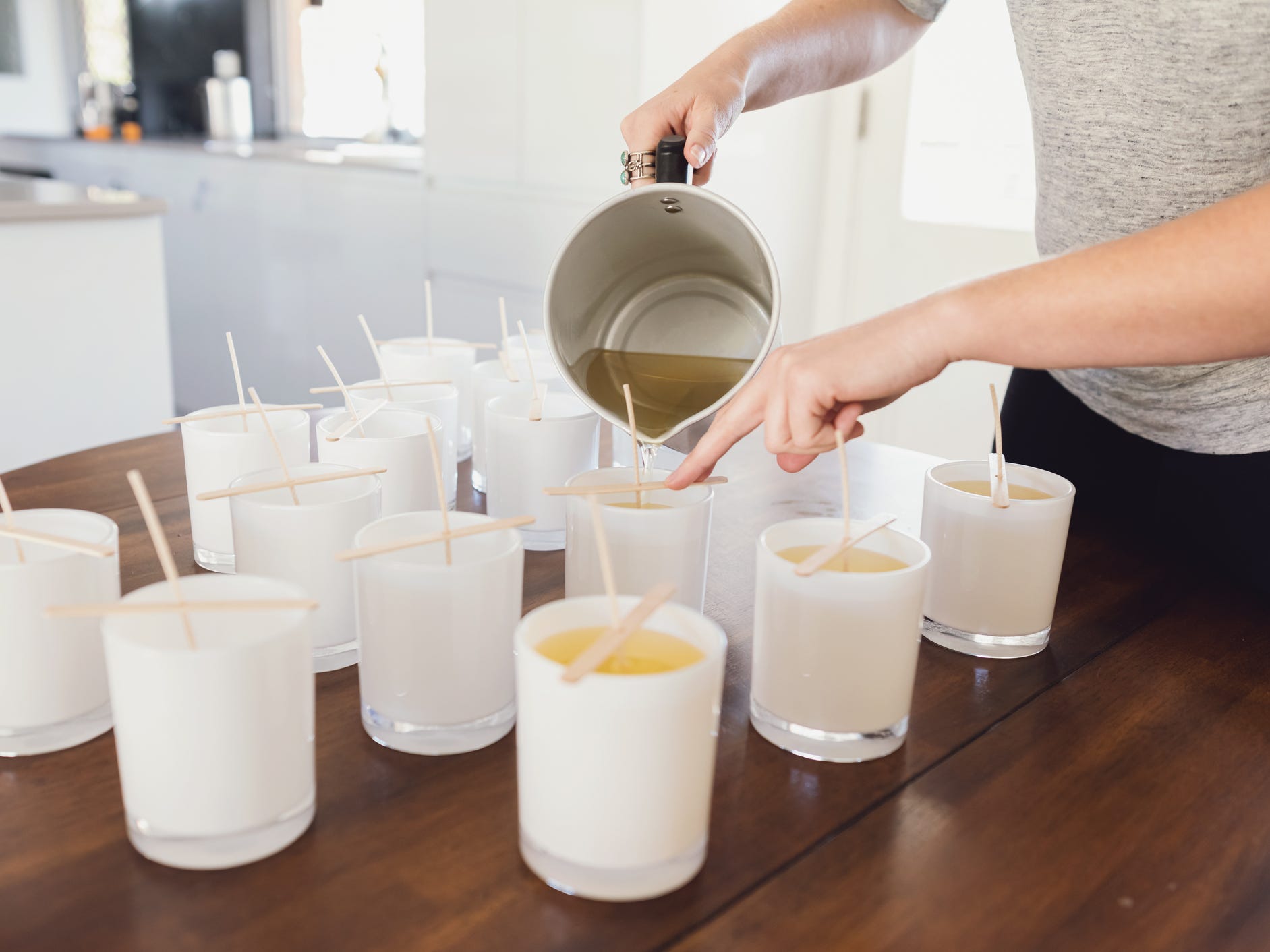 A person pouring melted wax into candle jars