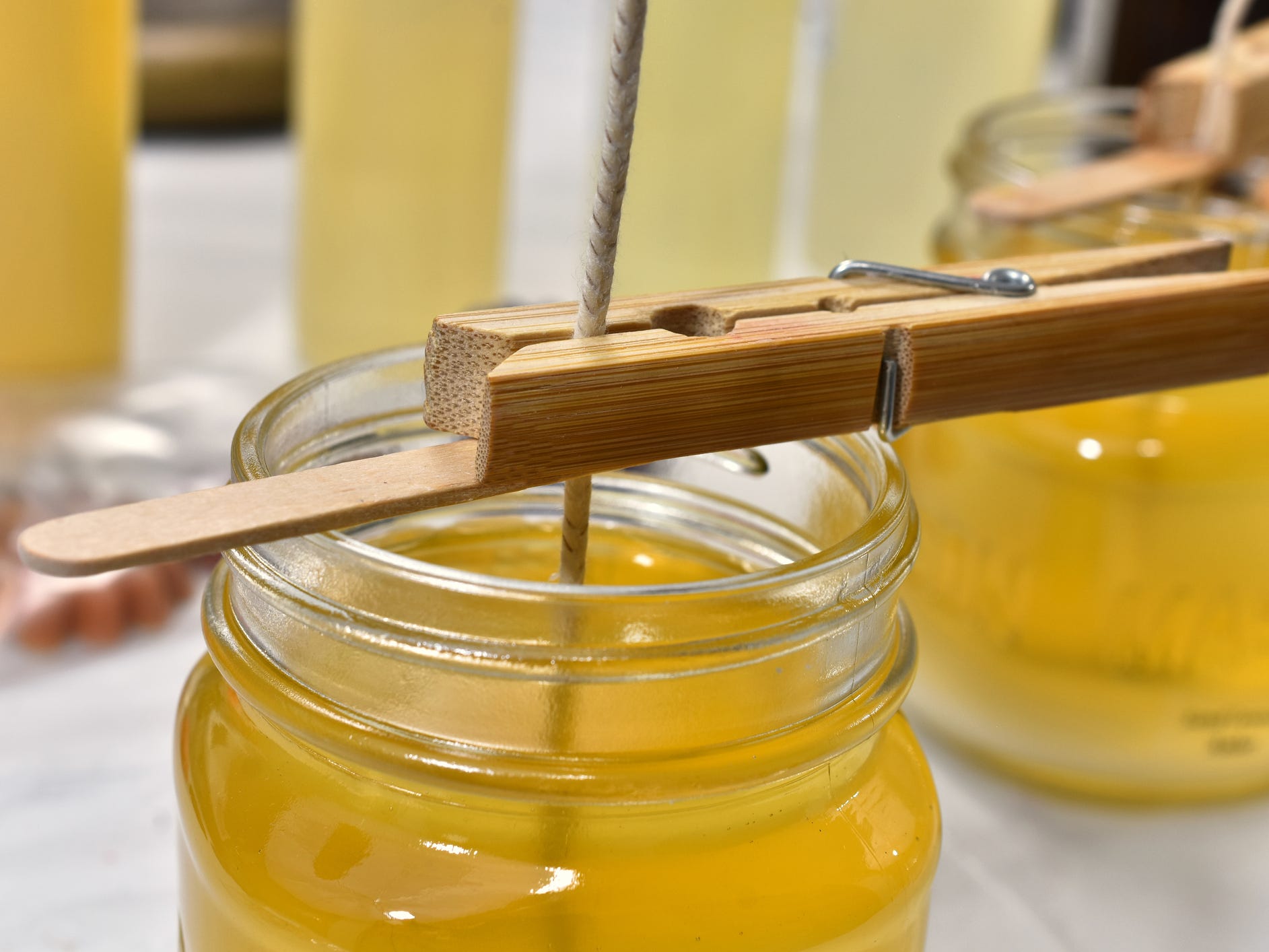 A jar full of melted candle wax with a wick sitting in it being held in place by a clothespin