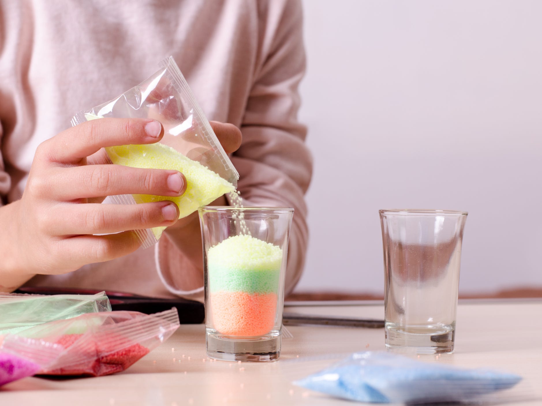 A person pouring different colored candle wax flakes into a glass cup