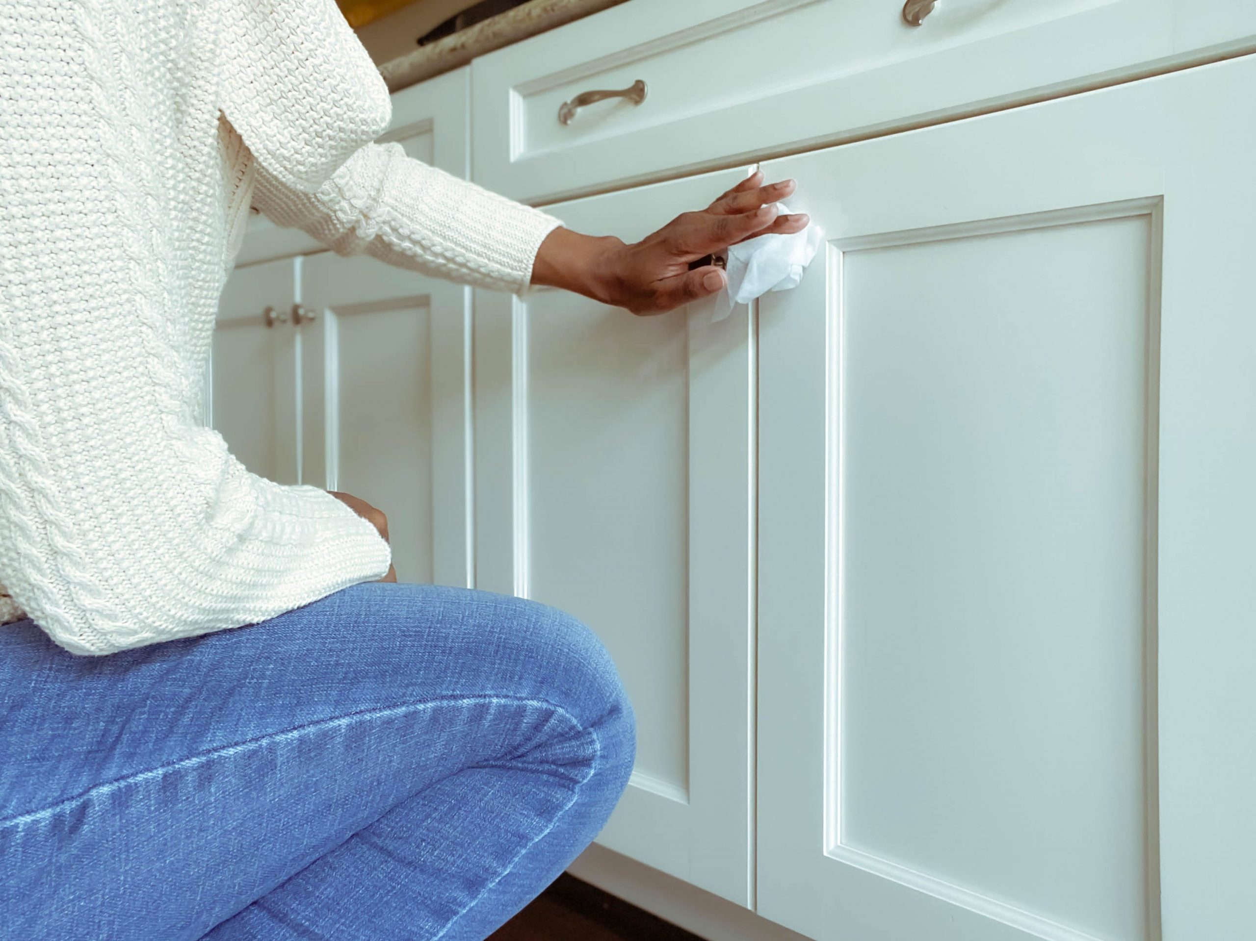 A person cleaning the handles of a kitchen cabinet