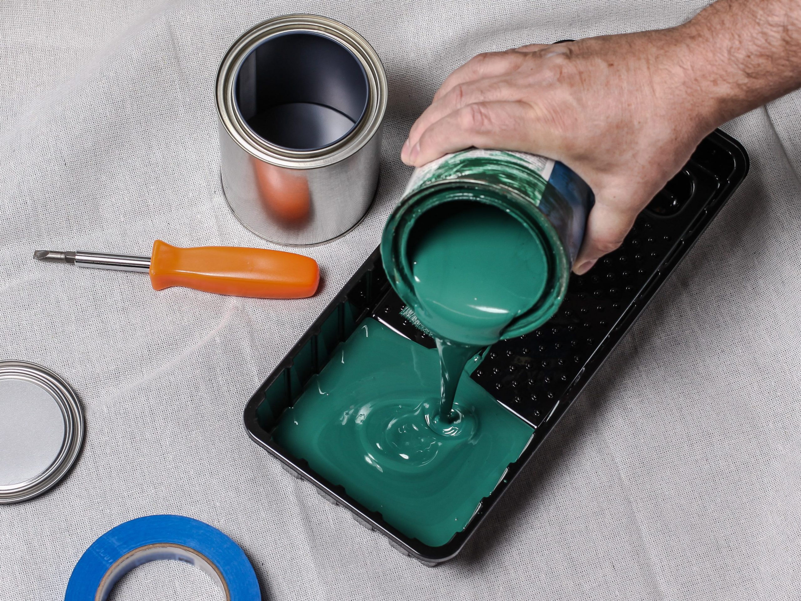 A closeup of a hand pouring dark green paint into a black paint tray