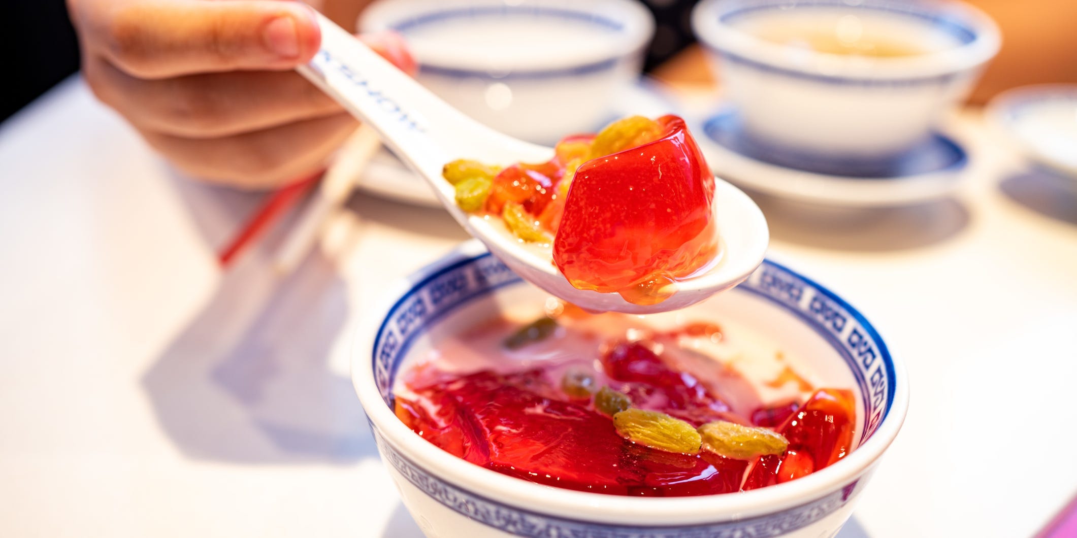 Person scoops a spoon full of red jello from a white bowl with blue trim.