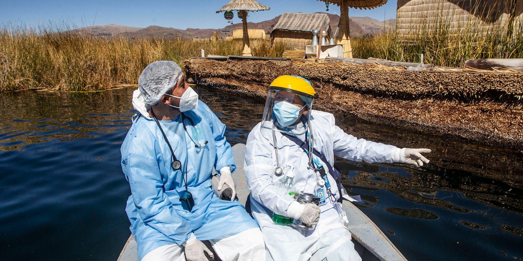 Two men in wearing protective equipment are on a boat on lake Titicaca on in Puno, Peru, on July 7, 2021.  in the background is the Uros Islands are made entirely from reeds