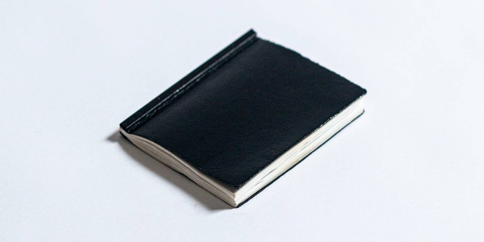 A small, black leather bound notebook laying down on a field of white.