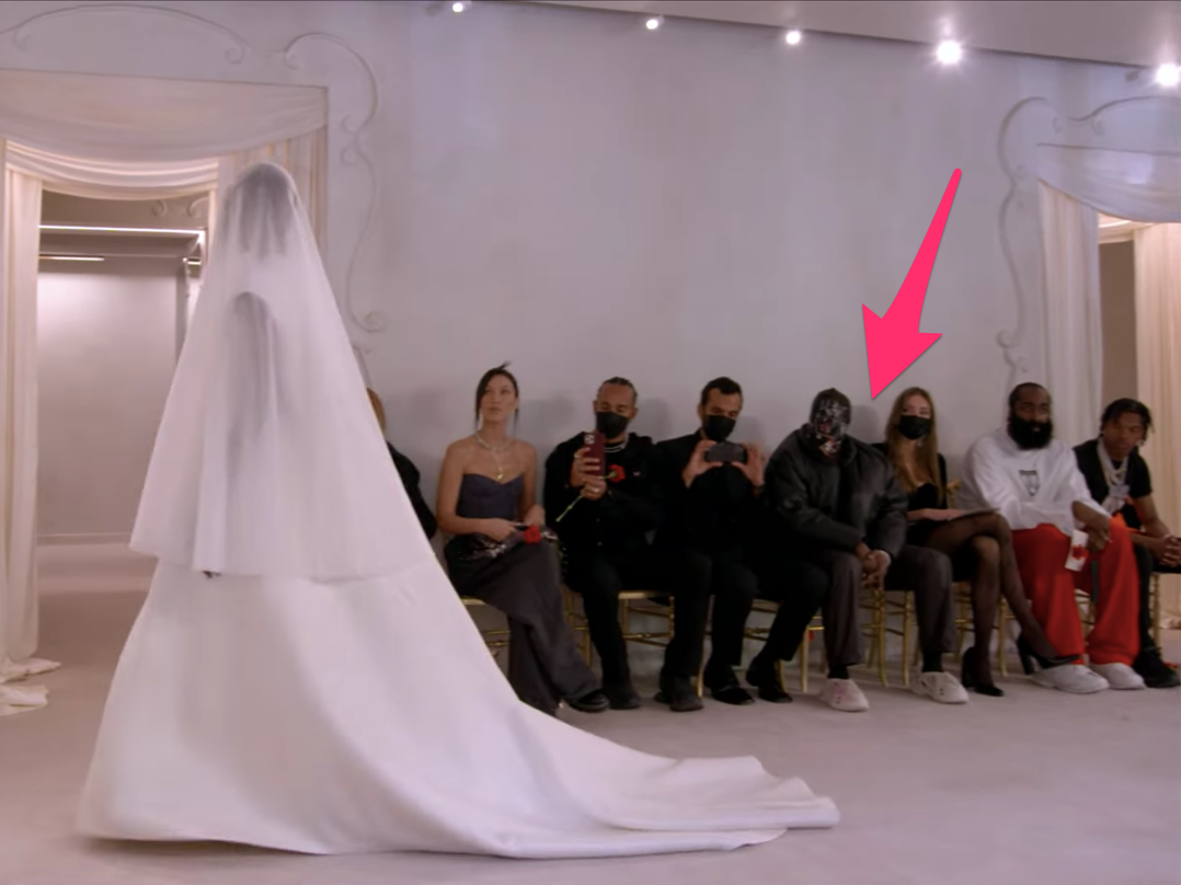 Kanye West seated at Balenciaga fashion show wearing Gap jacket