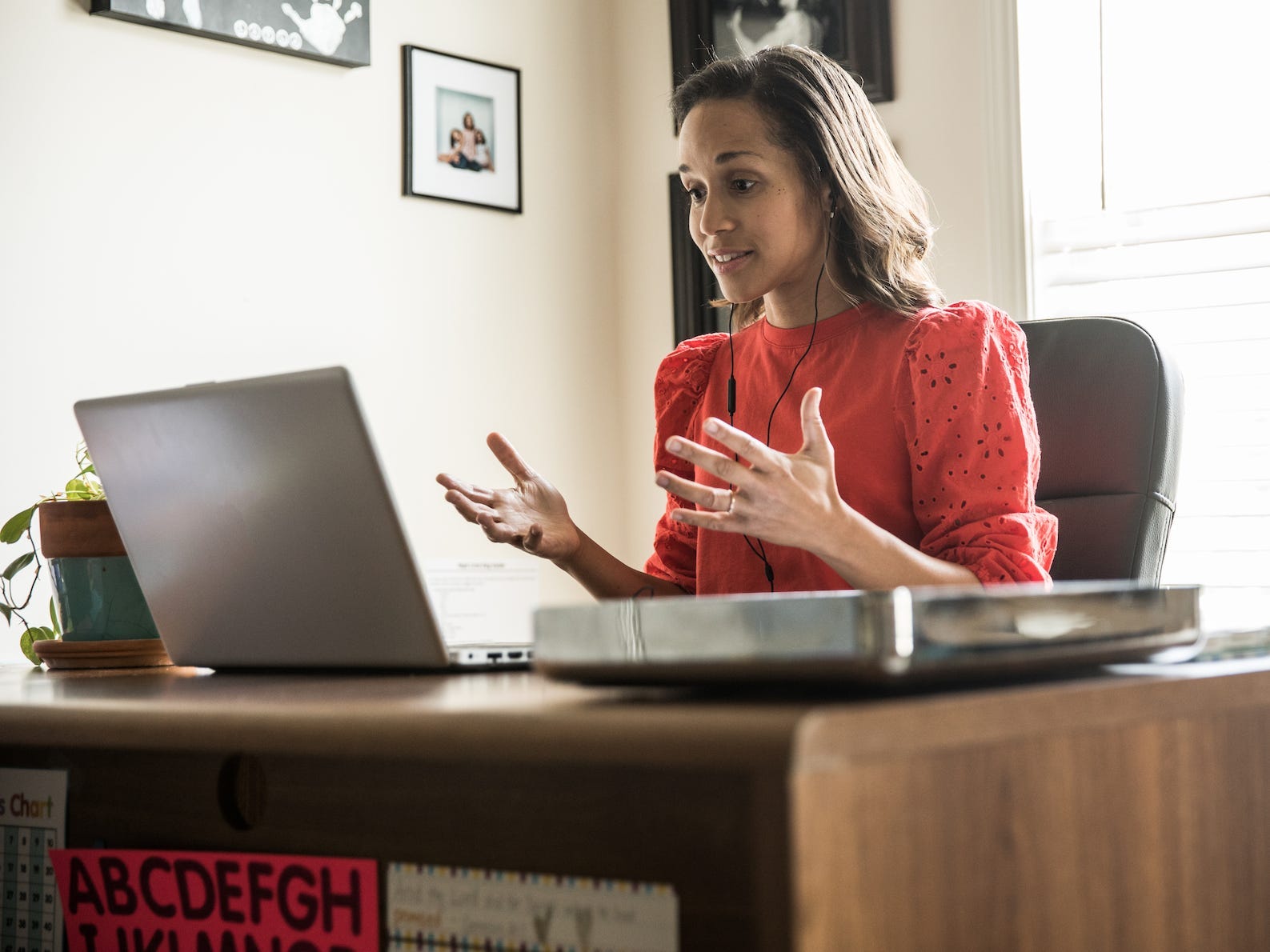 A woman is working in a home office. She is wearing headphones and talking to someone on her laptop