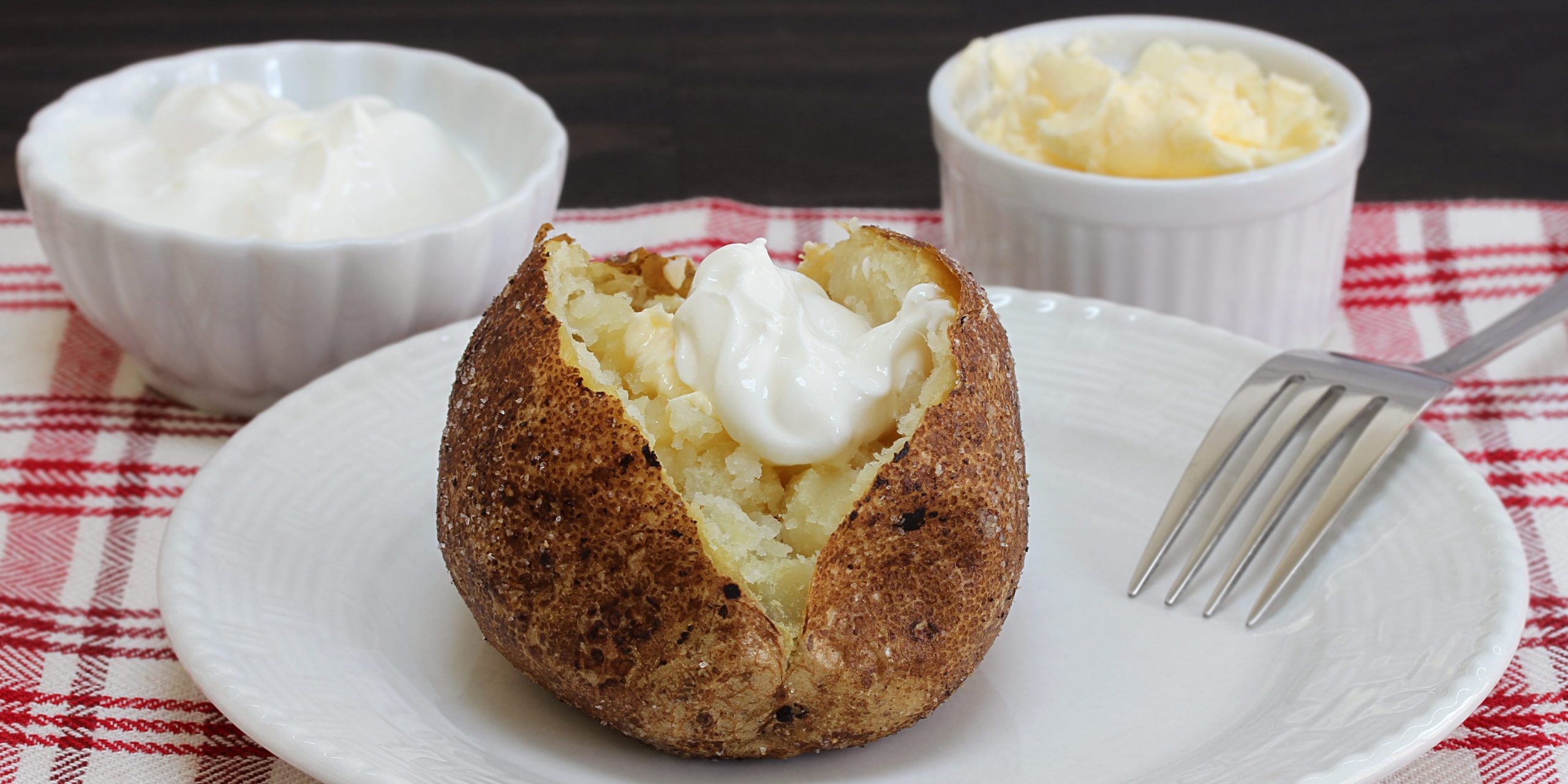 A baked potato topped with sour cream on a place with a fork