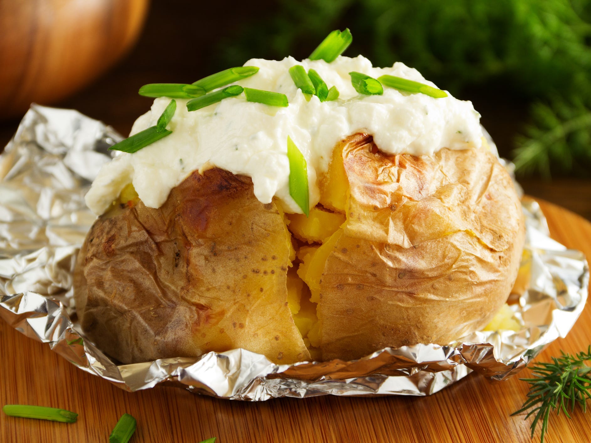 A baked potato sitting in foil topped with sour cream and chives