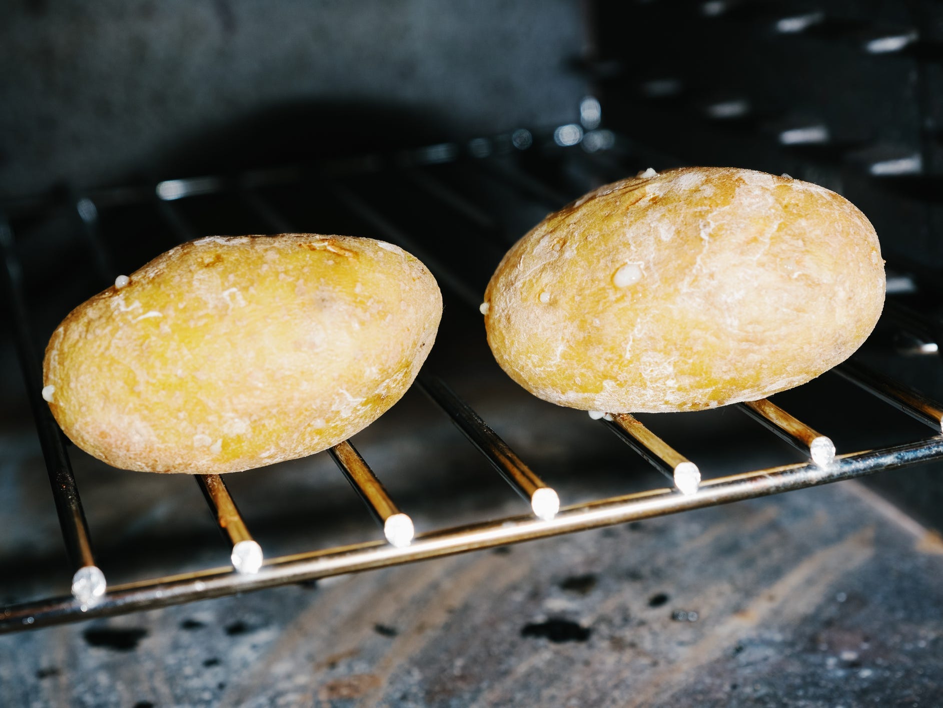 Two potatoes baking in an oven directly on the rack