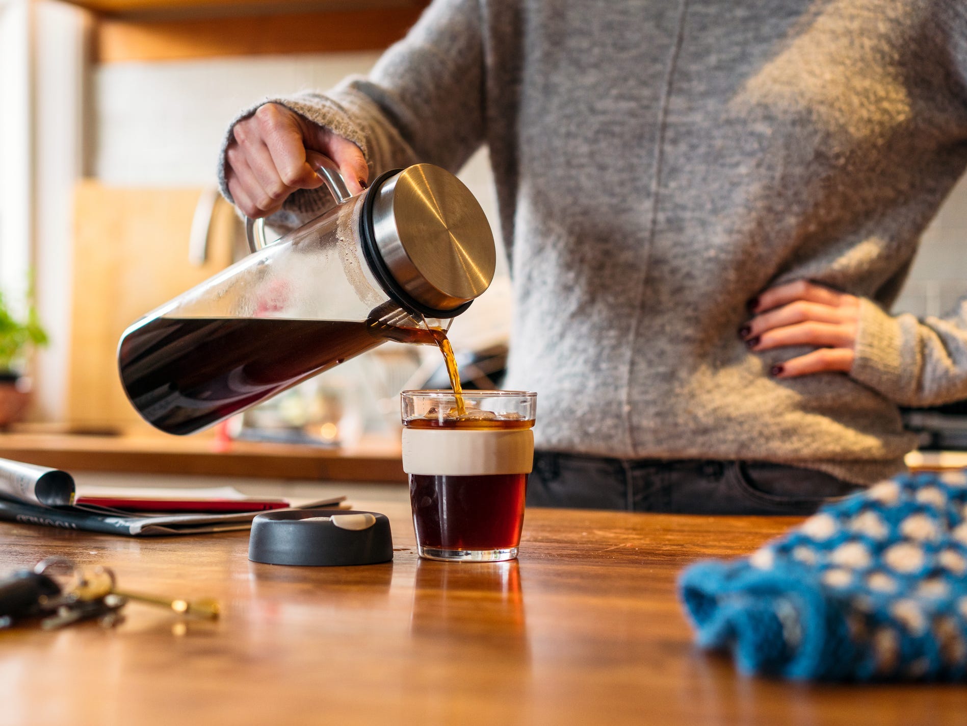 A person pouring cold brew out of a glass pitcher into a clear glass mug