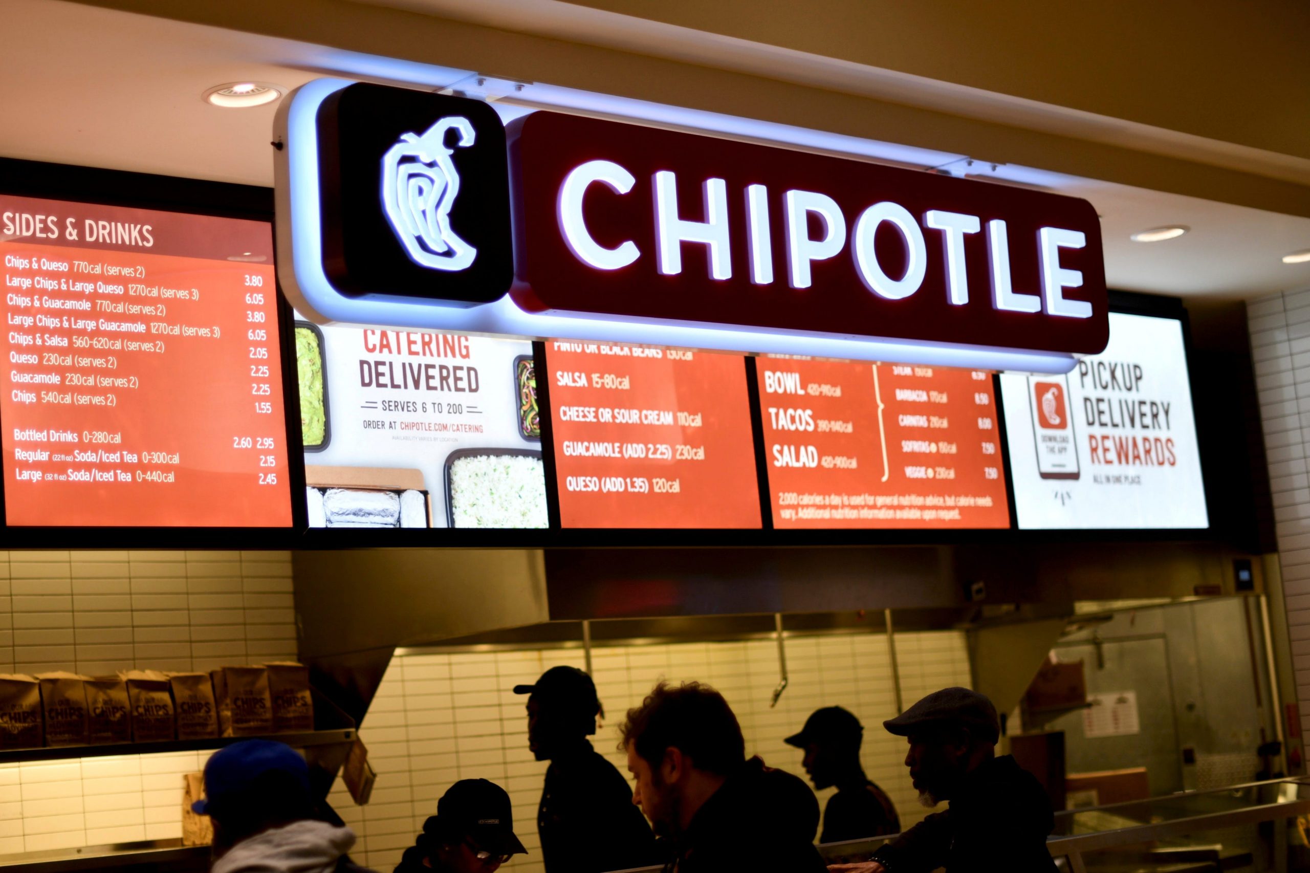 People crowd in front of a fast-food counter with a lighted Chipotle sign