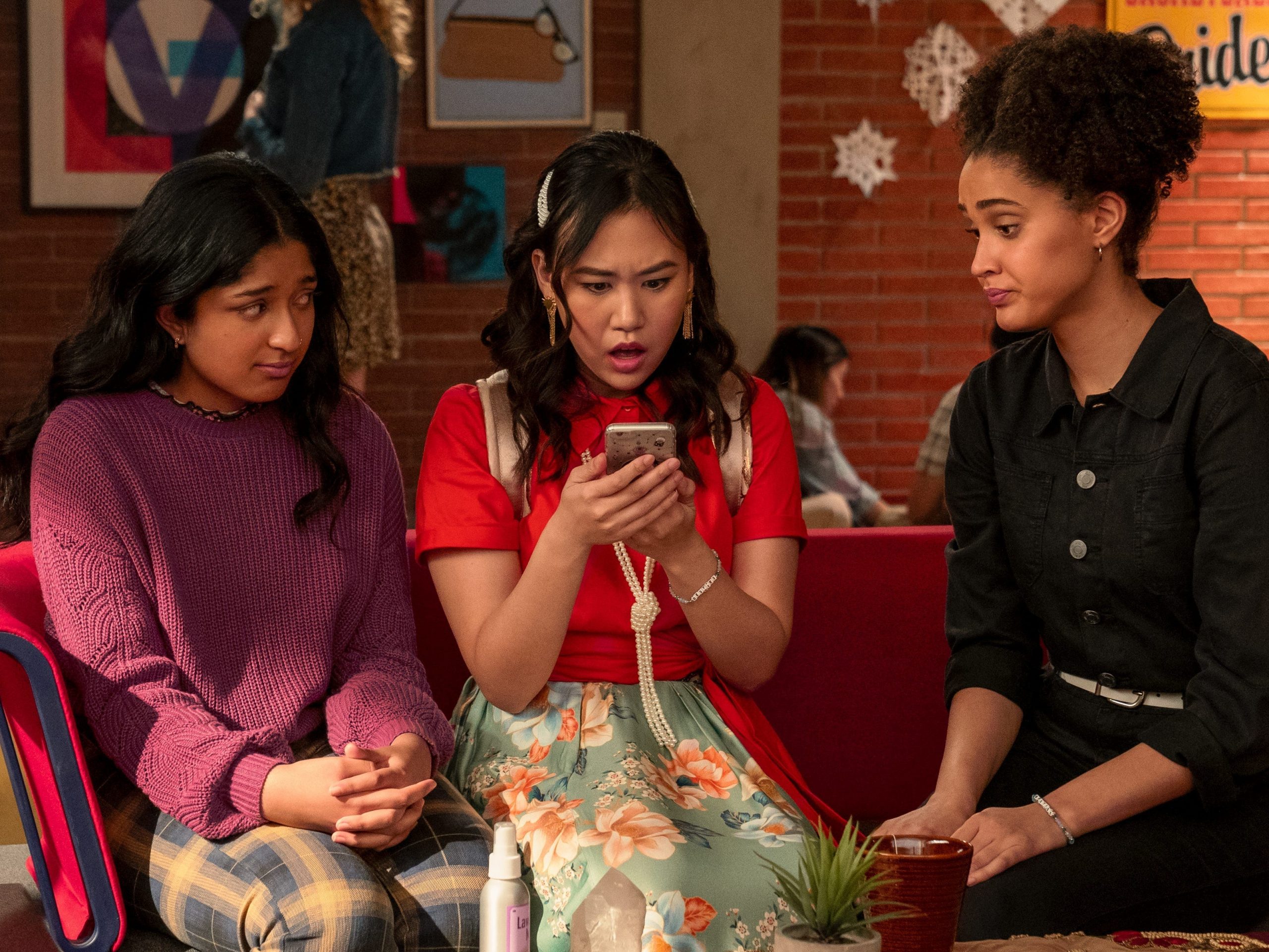 Maitreyi Ramakrishnan, Ramona Young, and Lee Rodriguez sitting on a couch and looking at a cell phone on season two of "Never Have I Ever."