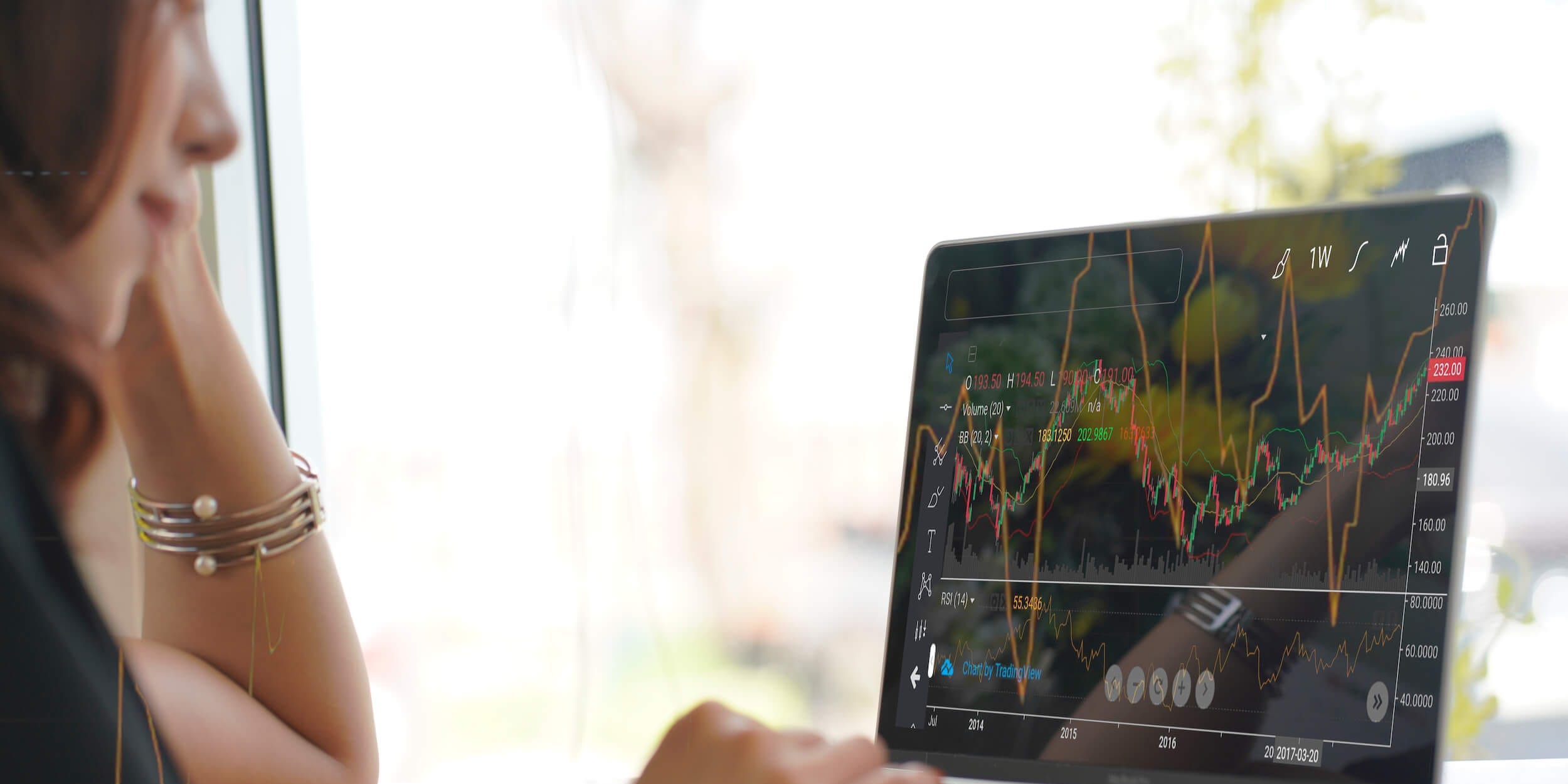 Asian woman looking at a stock market graph on a monitor screen.