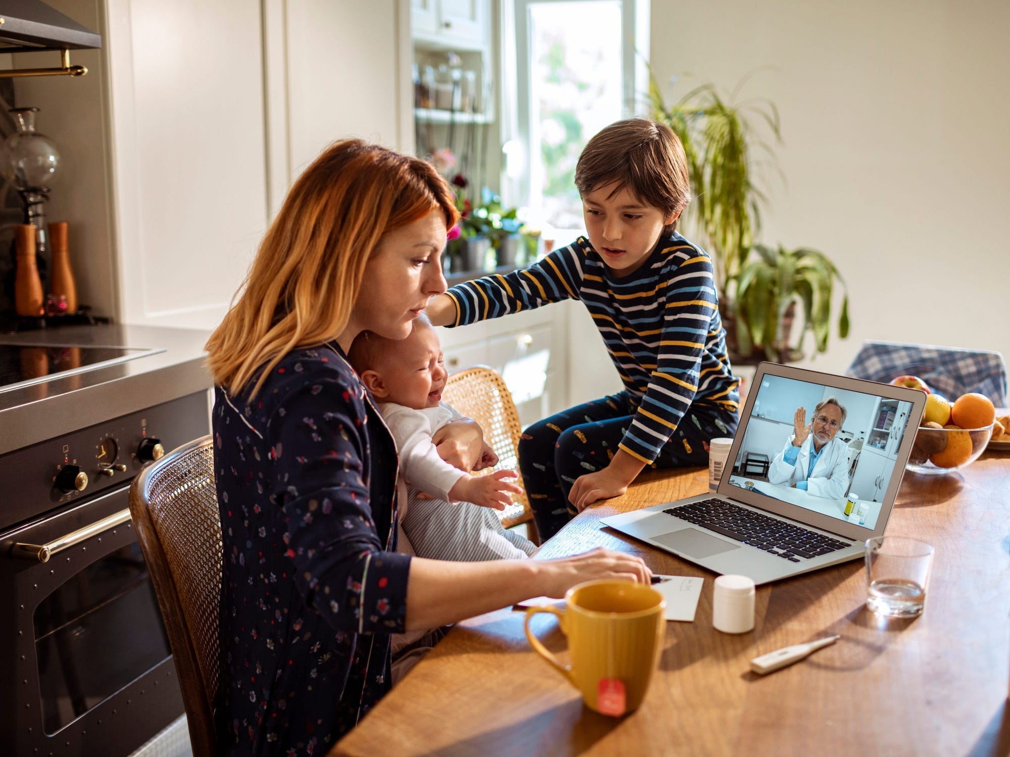 A woman and her two children sit at the counter looking at a computer for a telehealth appointment.