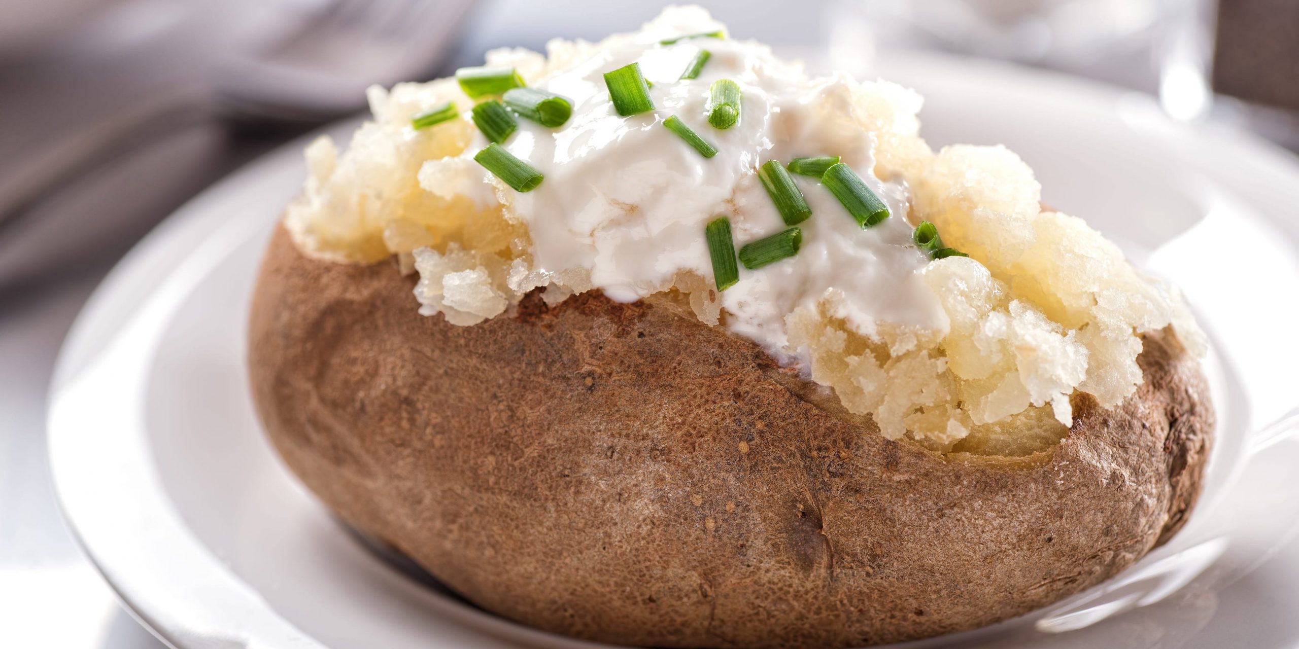 A baked potato cut open and topped with sour cream and chives