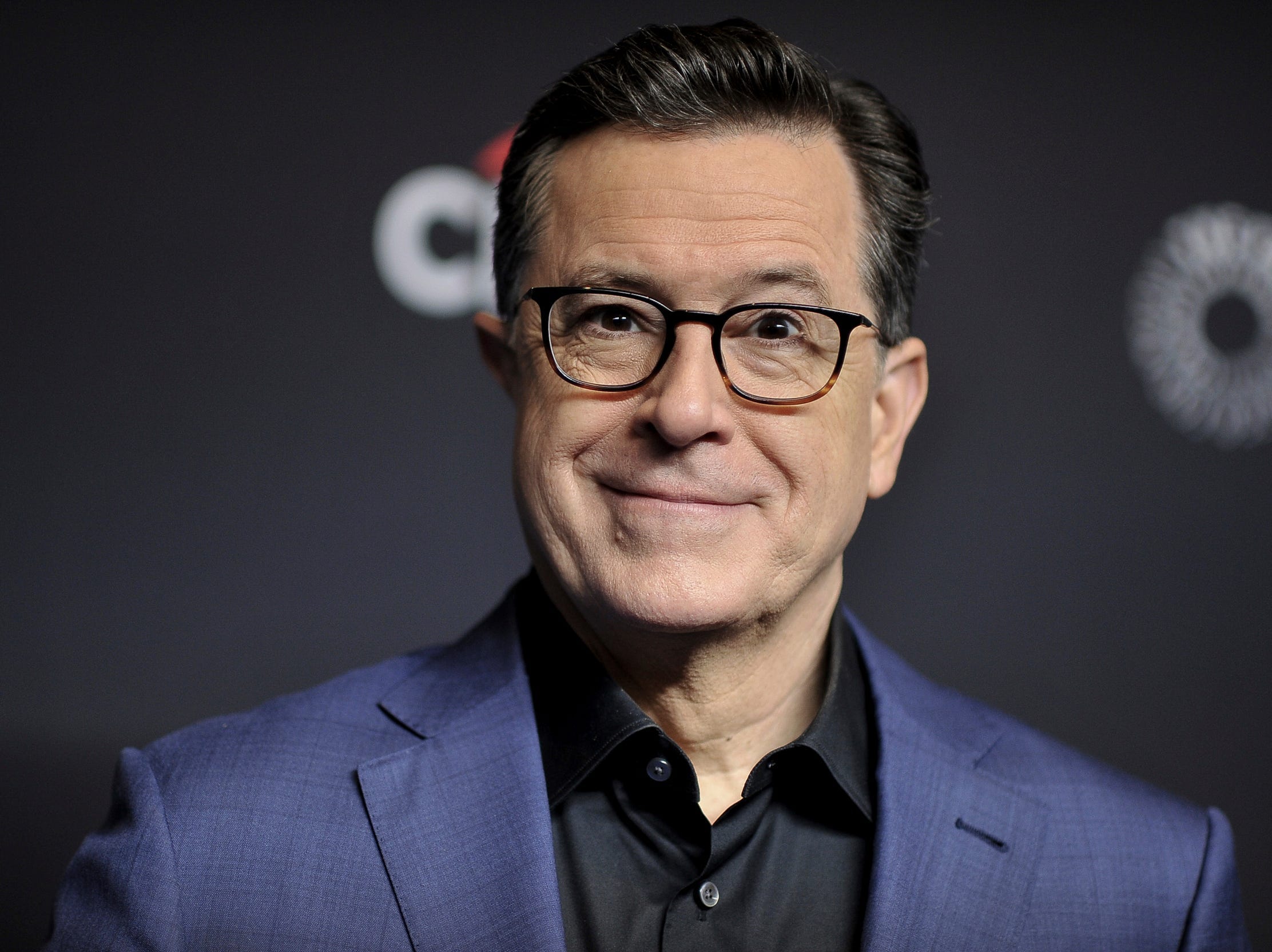 Stephen Colbert smiling in suit black background