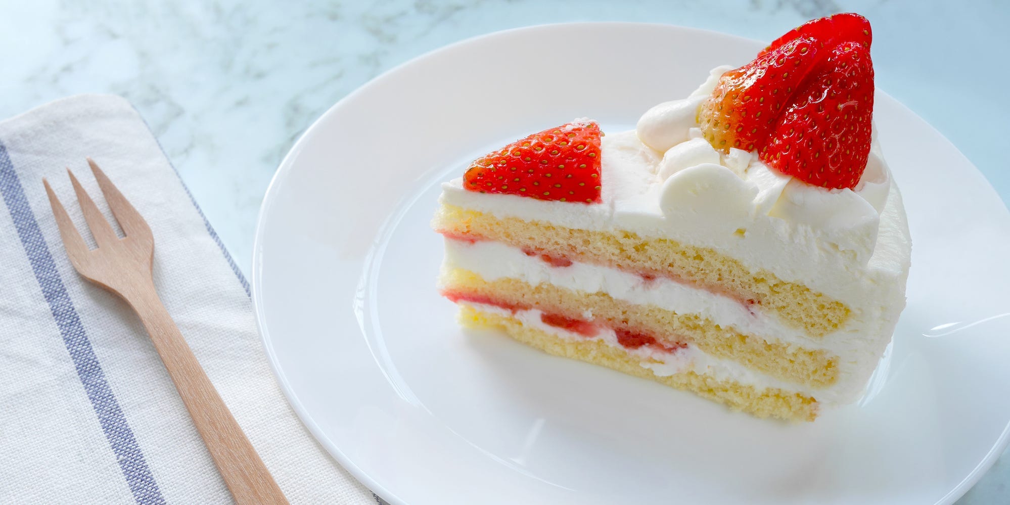 A slice of vanilla layer cake with strawberries and whipped cream frosting