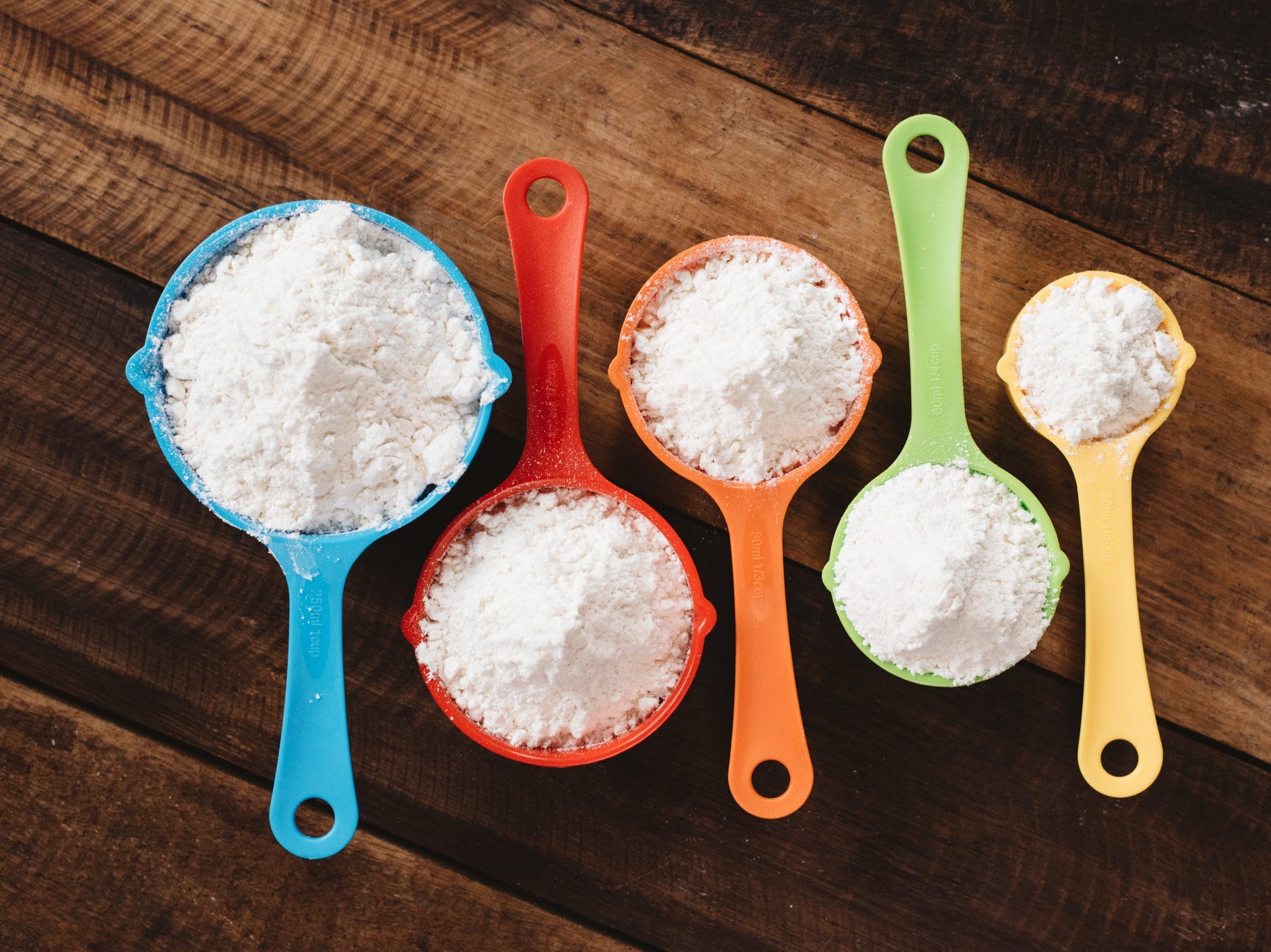 Colorful measuring cups full of flour lined up in a row