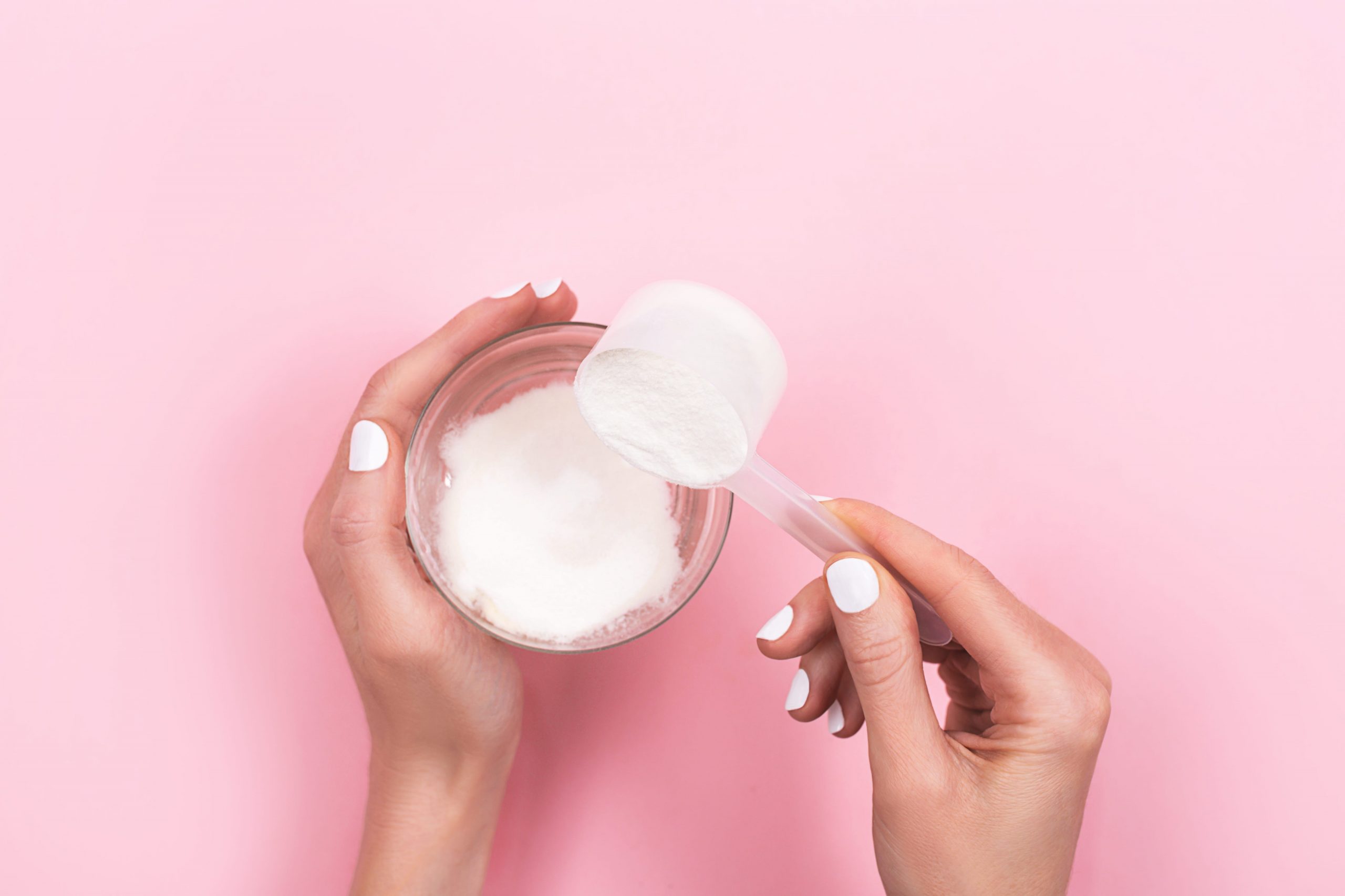 Hands pouring a scoop of collagen powder into a glass of water.