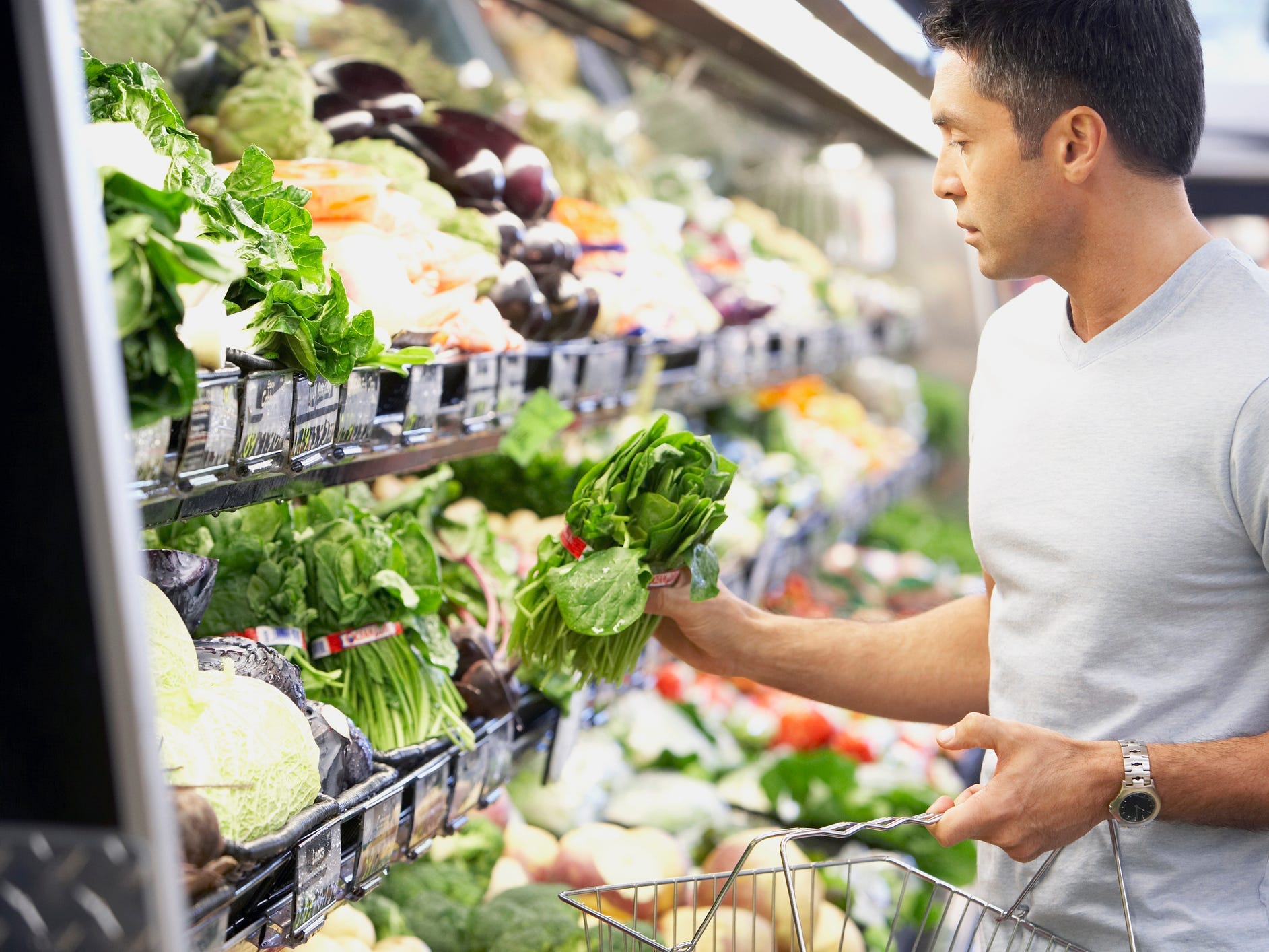 shopping for vegetables - a person in a white tee shirt holds leafy greens in a well-lit supermarket produce aisle.