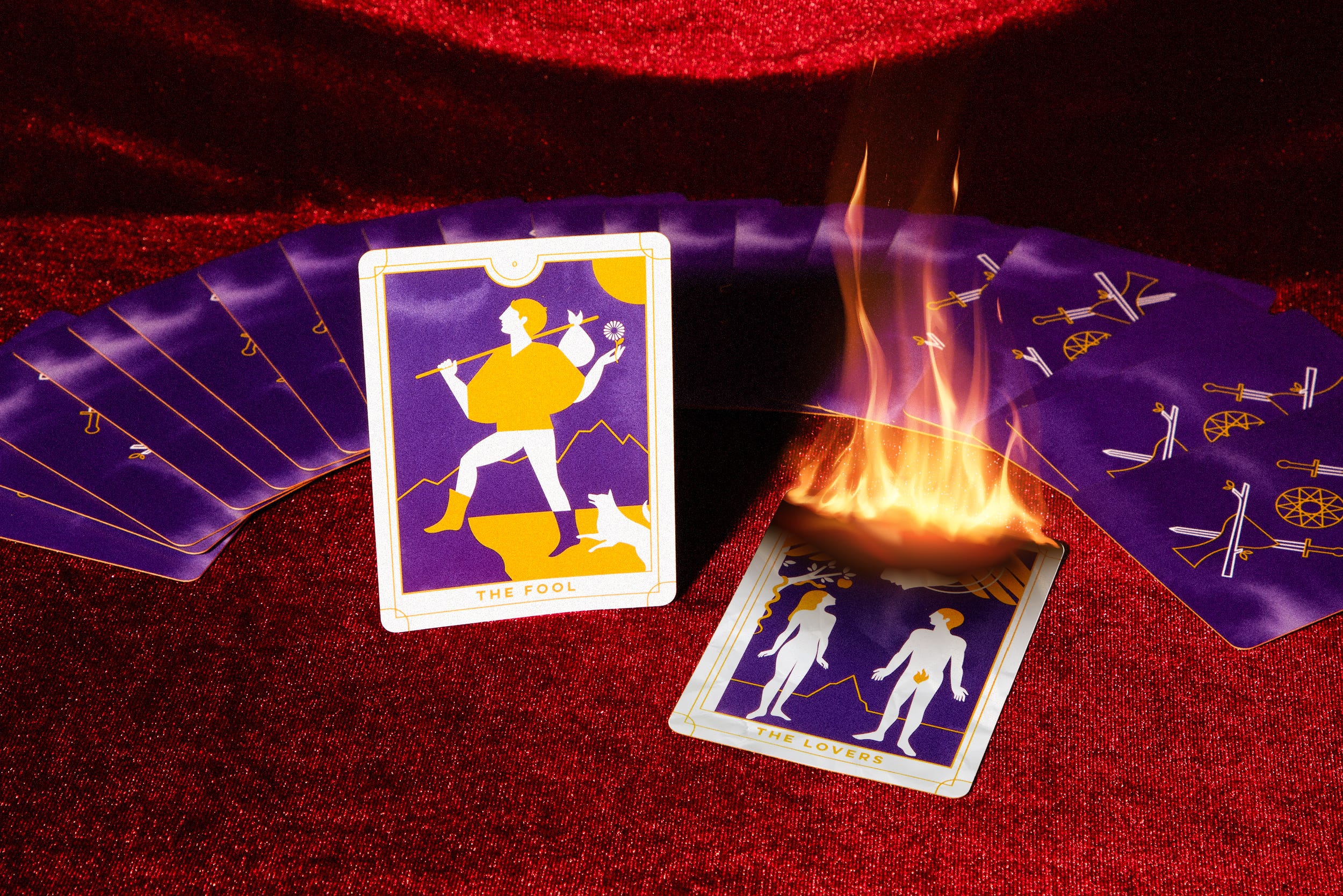 Tarot cards face down and spread out on a red velvet background with the The Fool card standing up and The Lovers card laying flat and face up on fire.