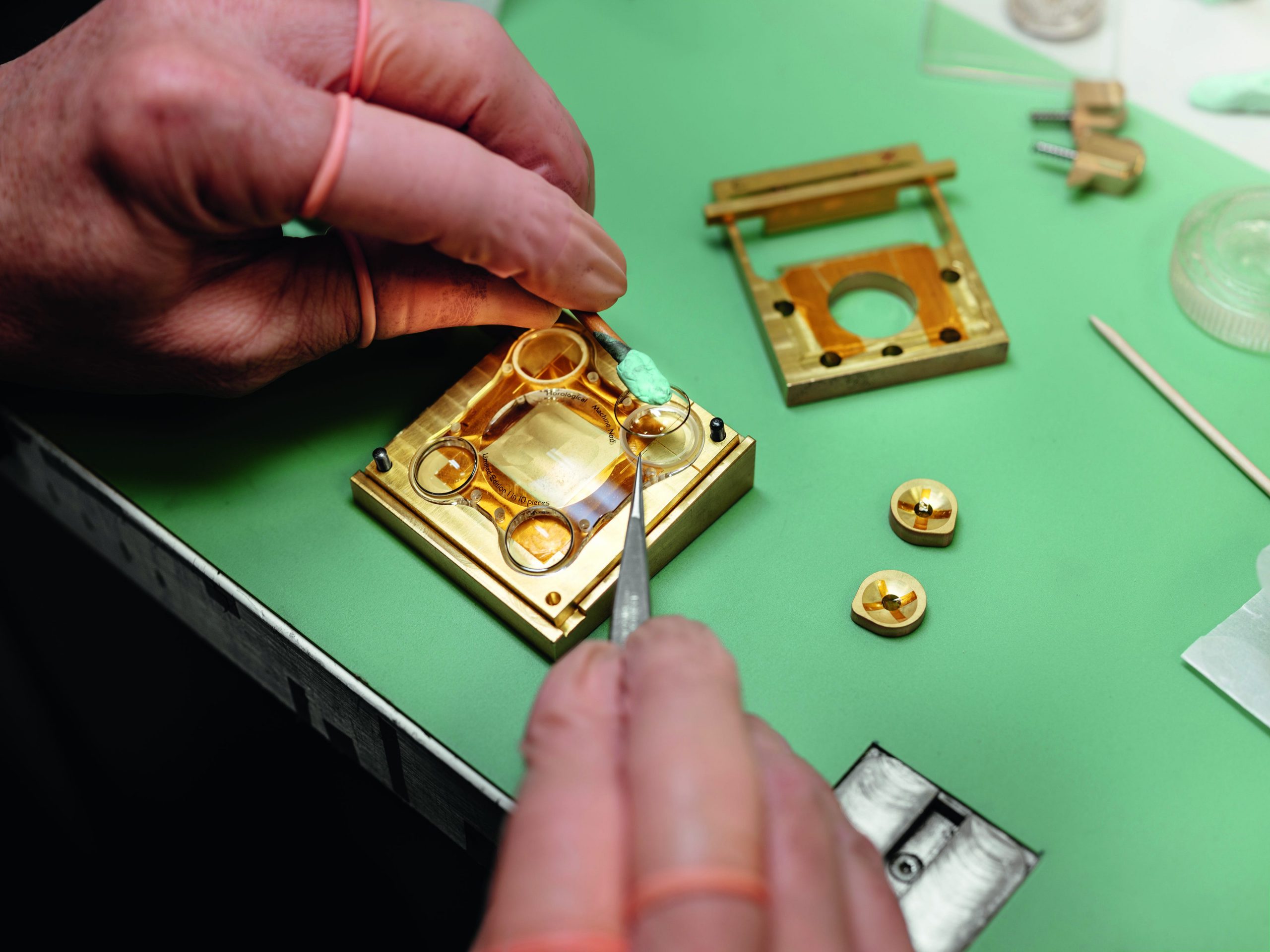 two hands making a gold watch on a green table