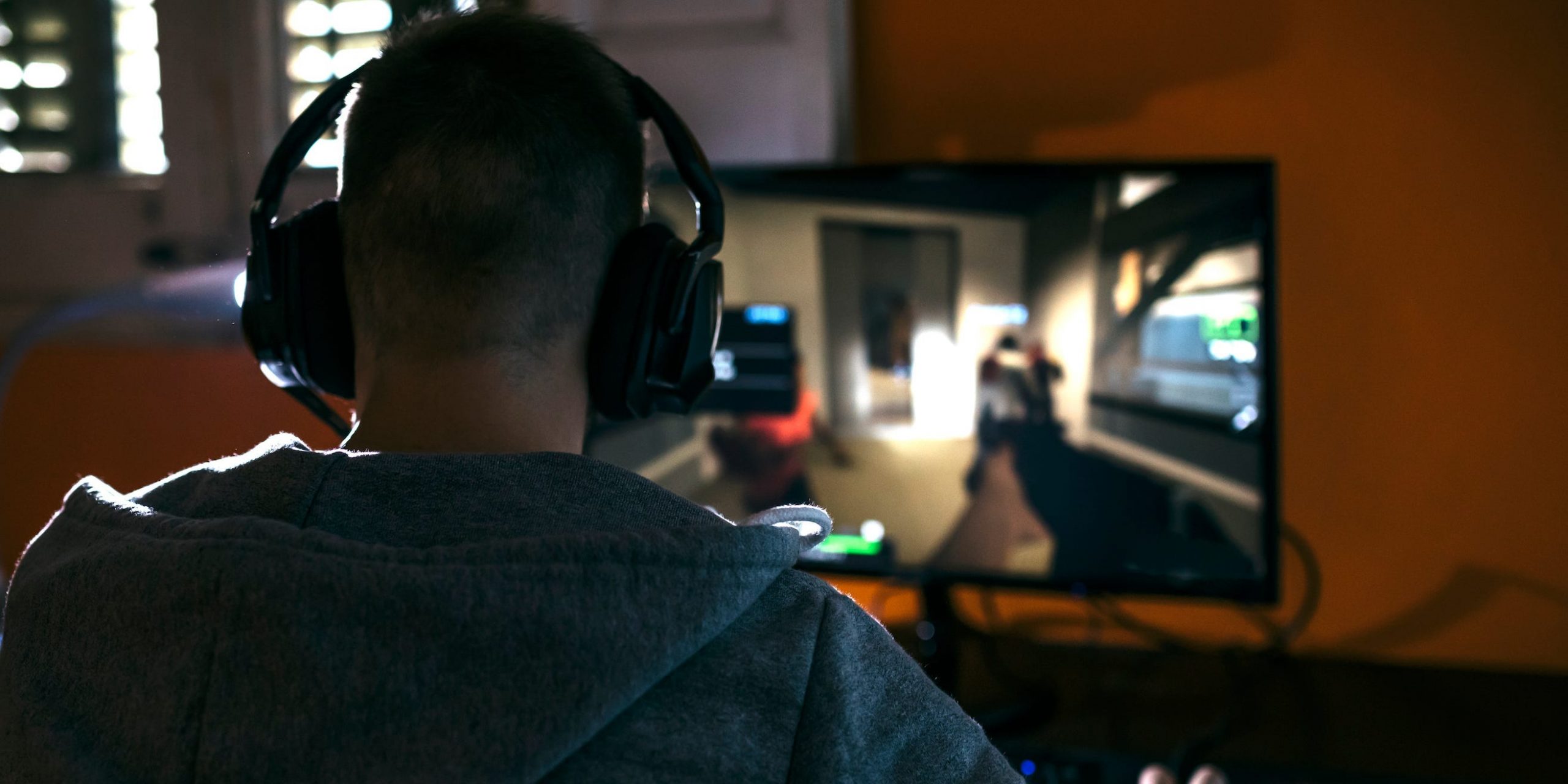 A man with headphones on plays a shooting game on his Windows PC computer.