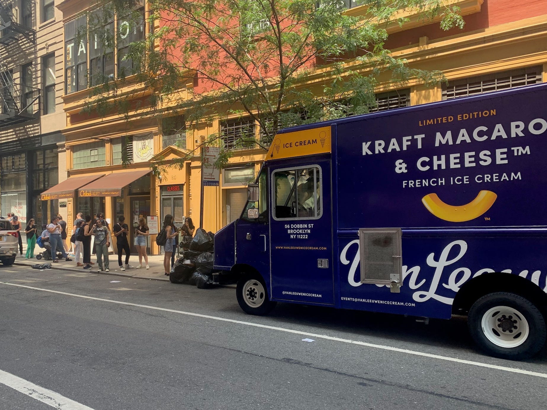 A New York street with people lined up in front of a navy ice cream truck.