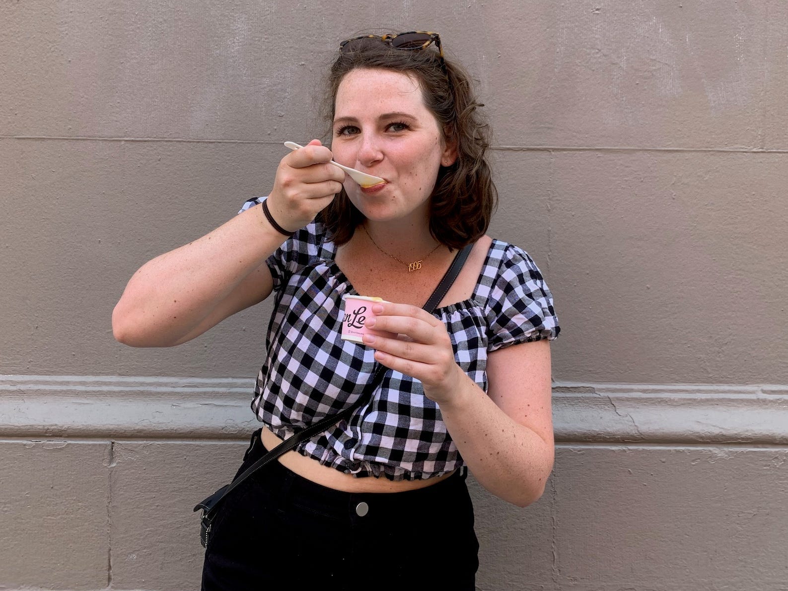 A brown haired woman eats a bite of ice cream in front of a gray wall.