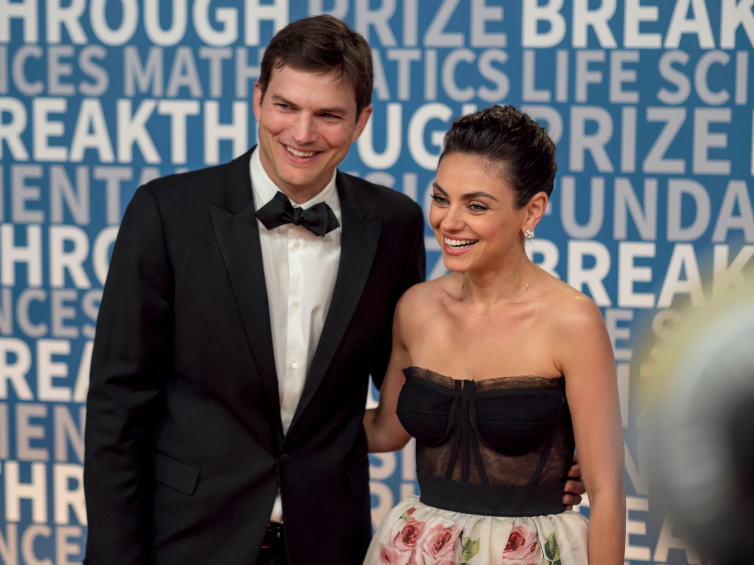 Ashton Kutcher with his arm around Mila Kunis on the red carpet