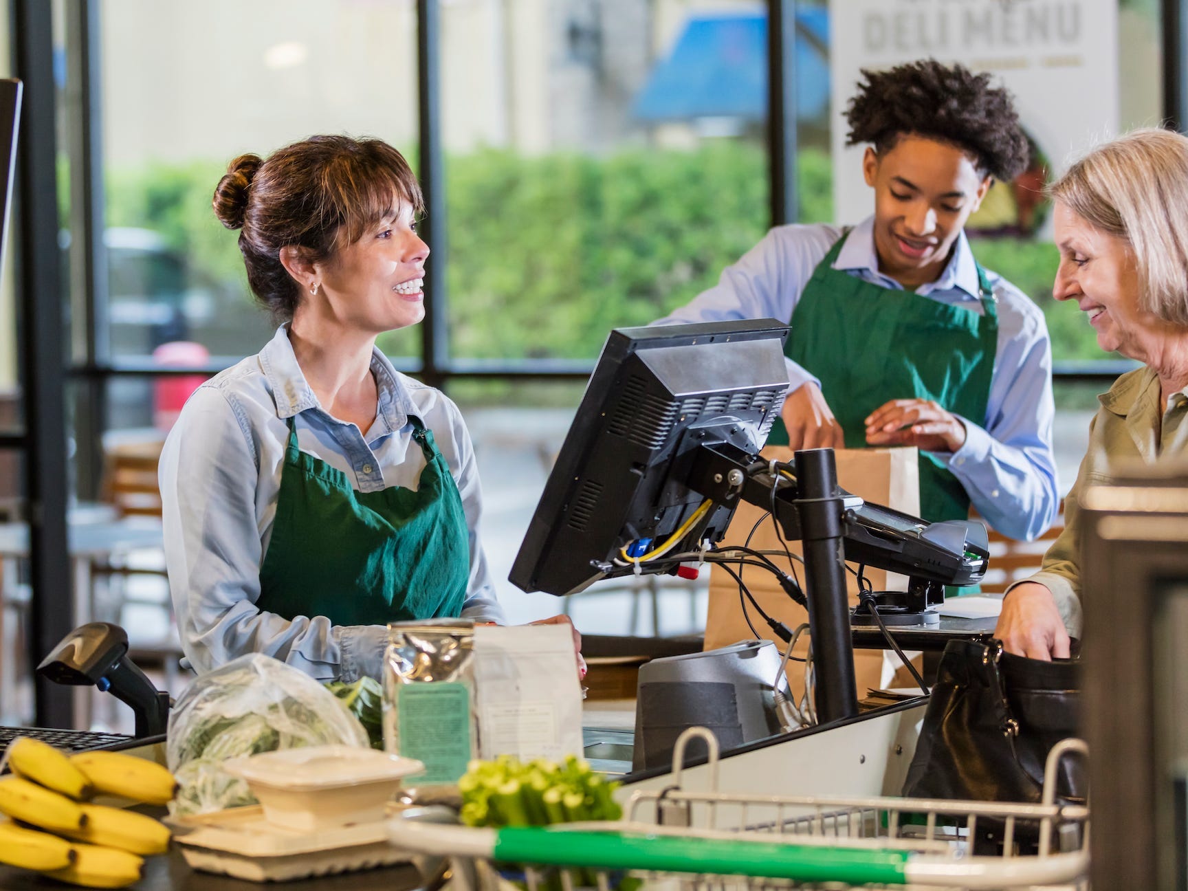 A customer and two employees at a supermarket checkout lane.