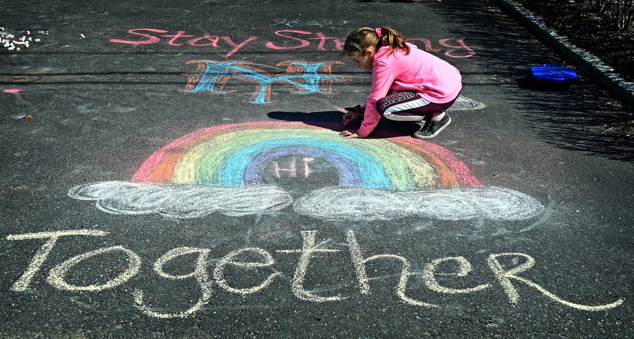 young girl drawing rainbow in chalk with word 'together' underneath it