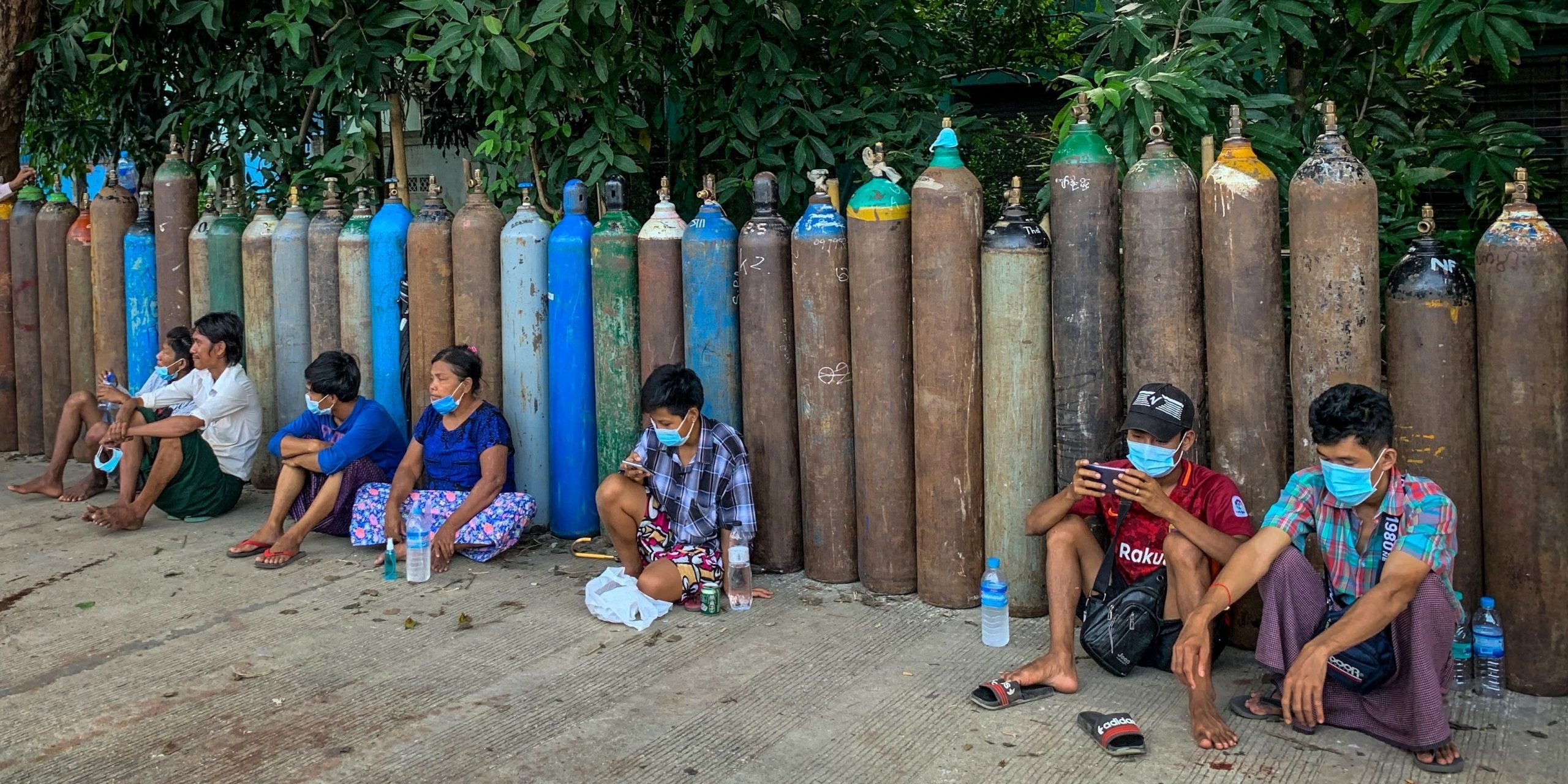 Myanmar residents sit in front of empty oxygen canisters waiting in line to fill up.