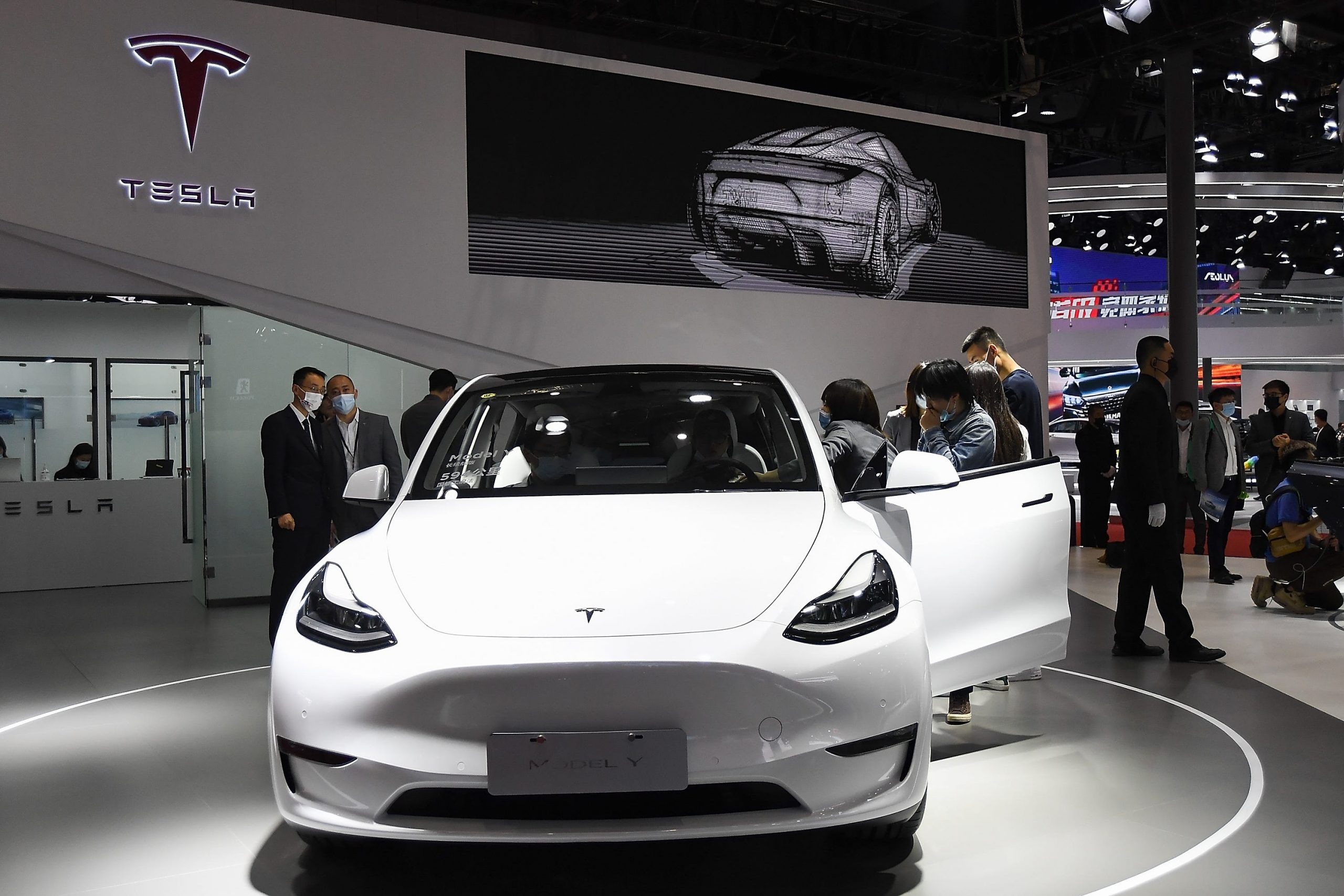 A white Tesla Model Y sits in a showroom with people walking around it.