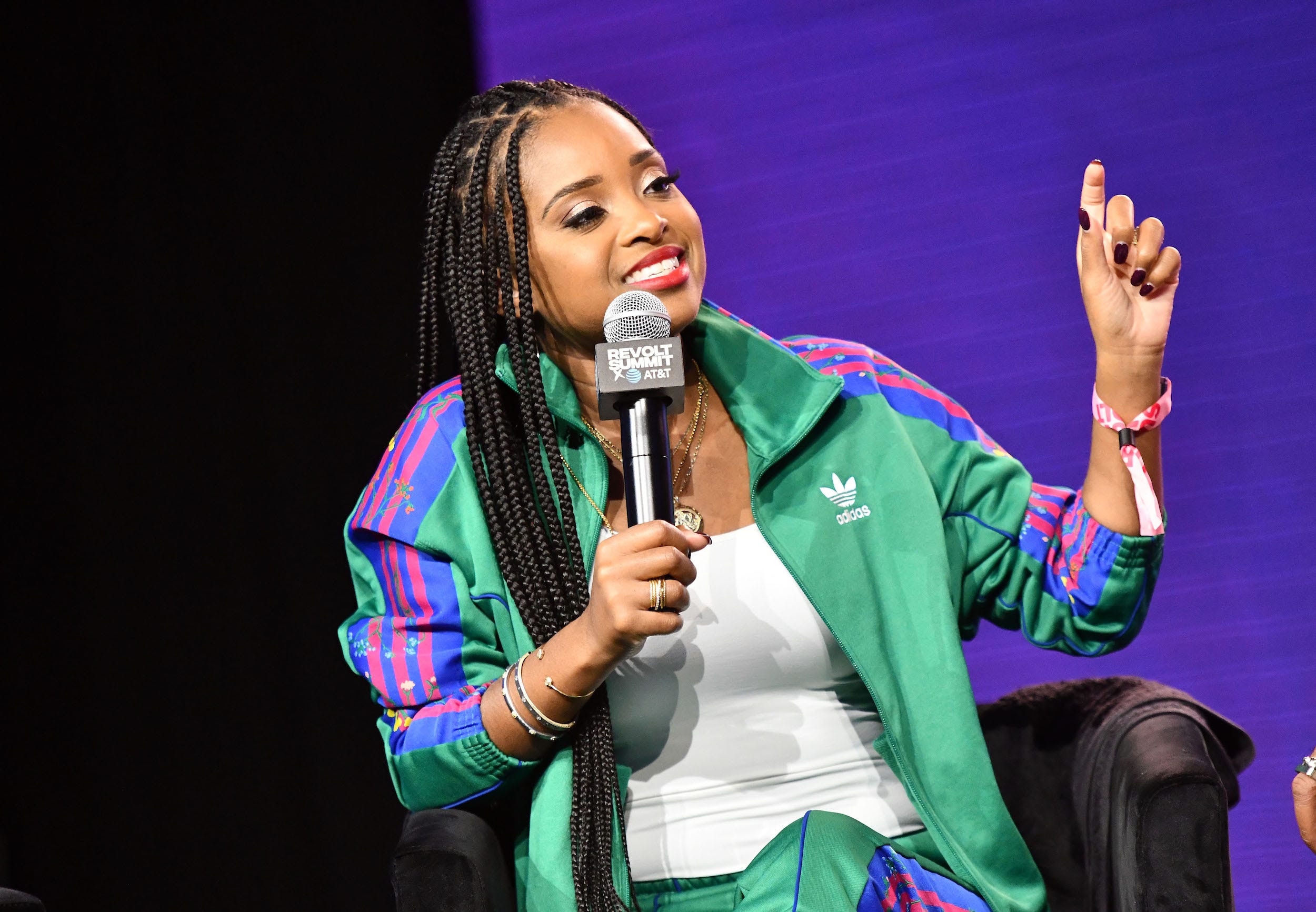 Tamika Mallory speaks into a microphone with a bright purple screen behind her.