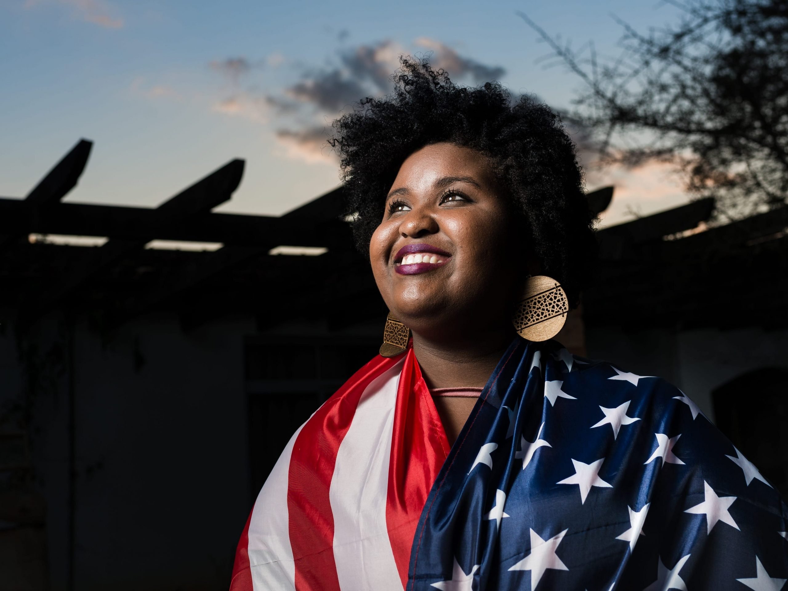 Black immigrant woman smiling while draped in American flag