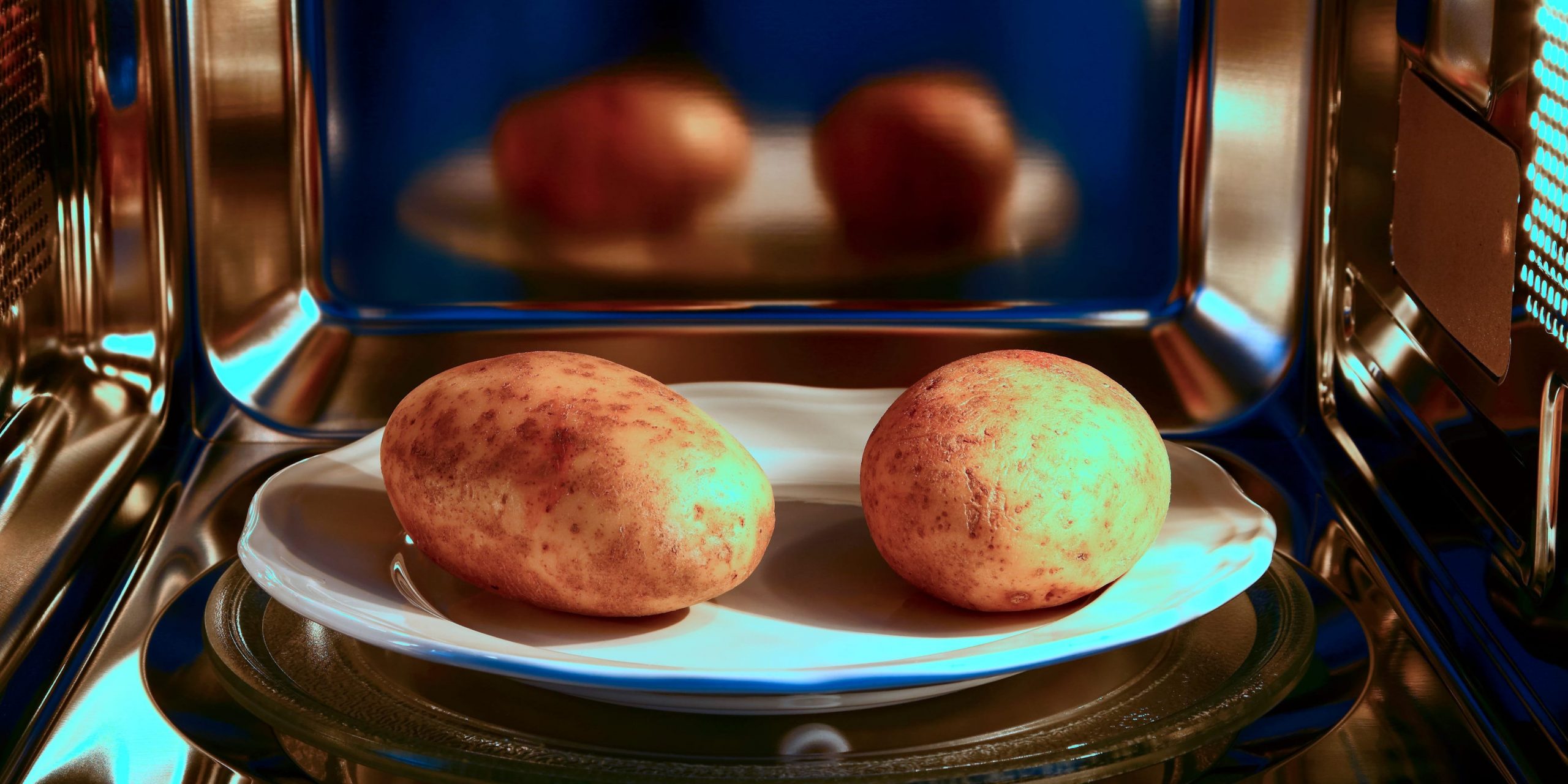 Two potatoes sitting on a white plate inside a microwave