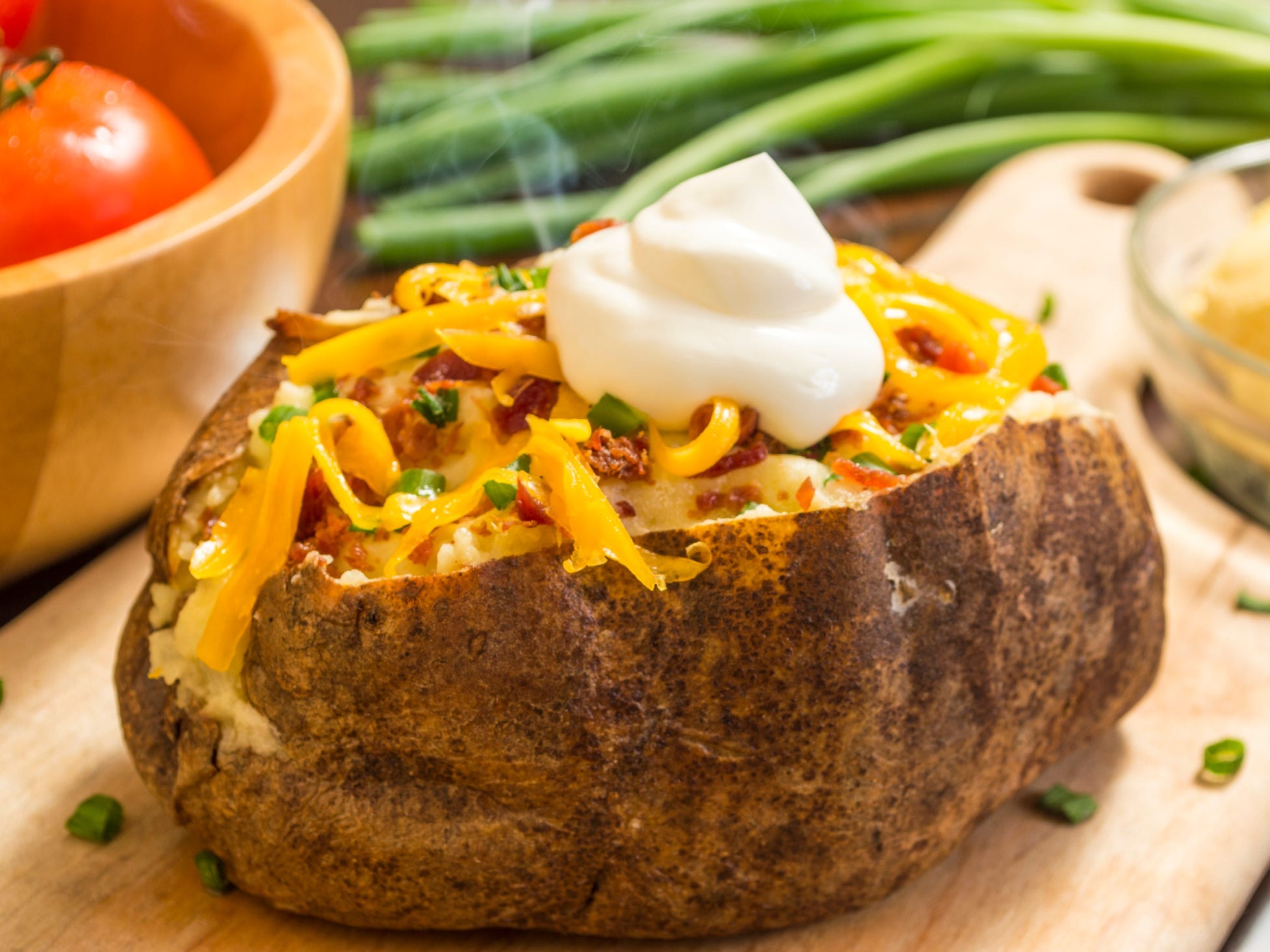 A baked potato split open and topped with cheese, bacon, and sour cream