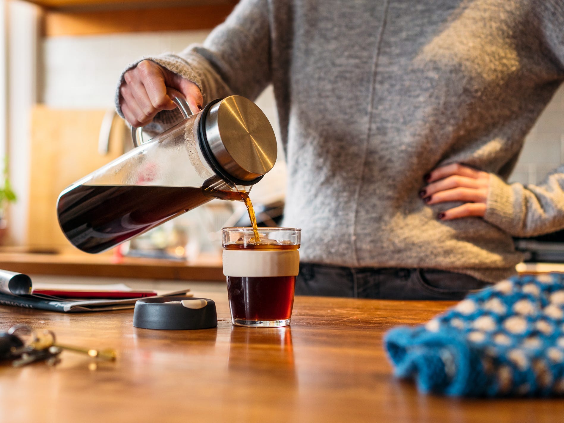 A person pouring cold brew out of a glass pitcher into a clear glass mug