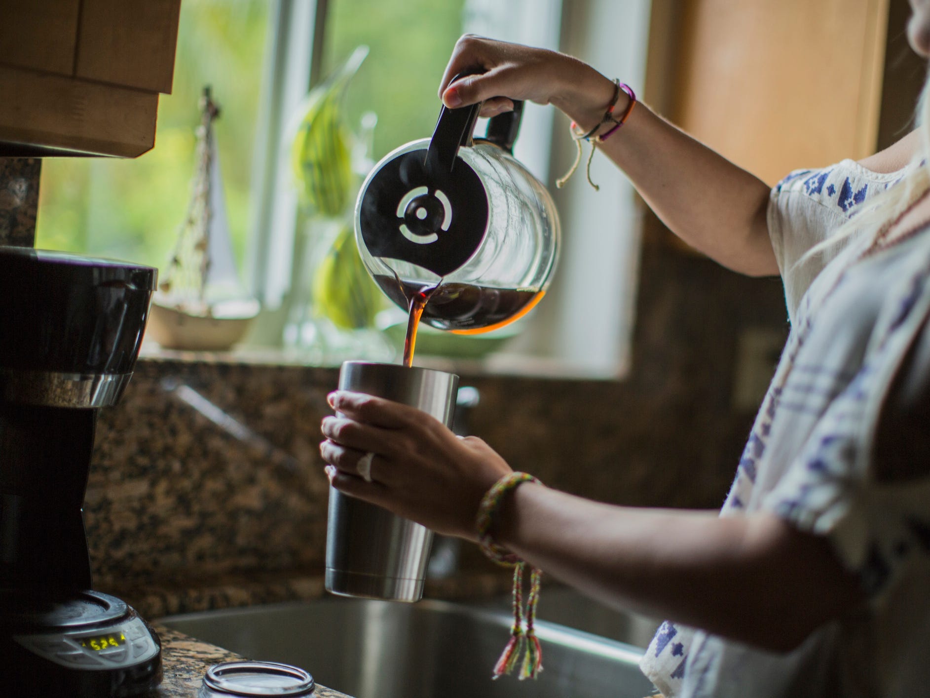 A woman pouring coffee out of a pot into a travel mug