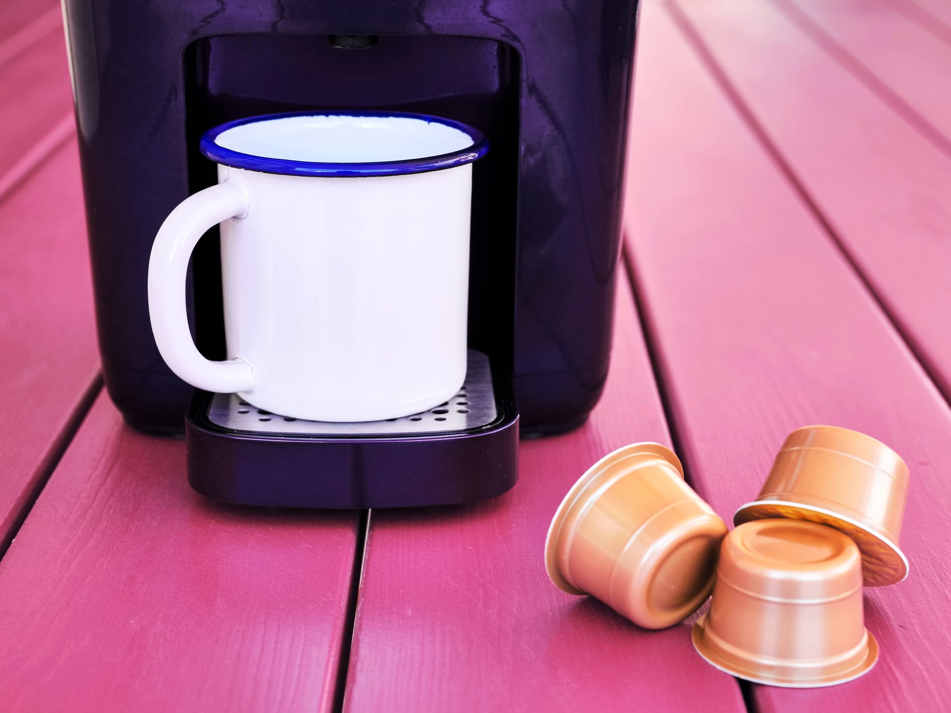 A Keurig-style coffee maker with a white mug sitting in it and three coffee pods next to it