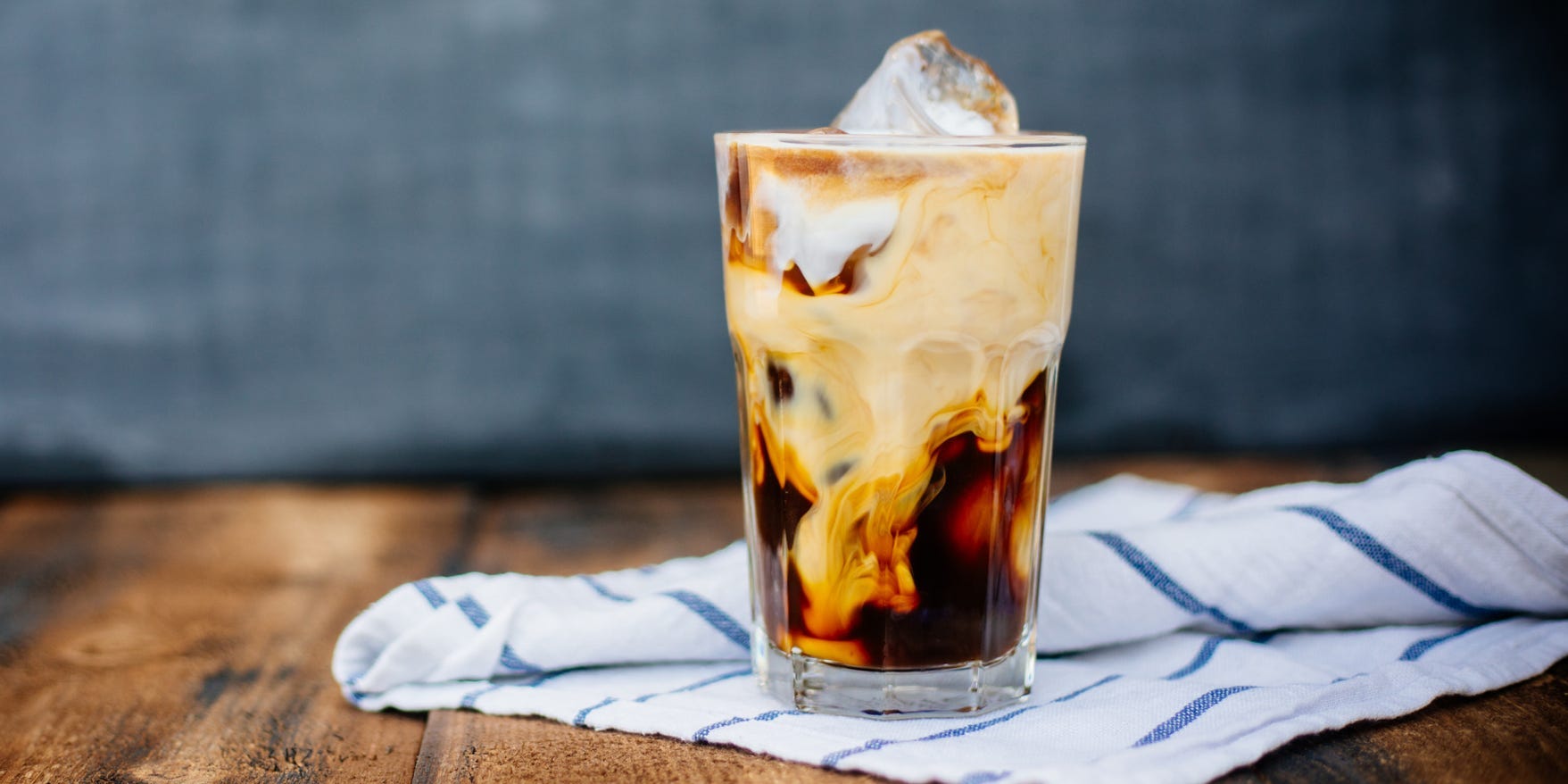 A glass of iced coffee with milk partially mixed into it