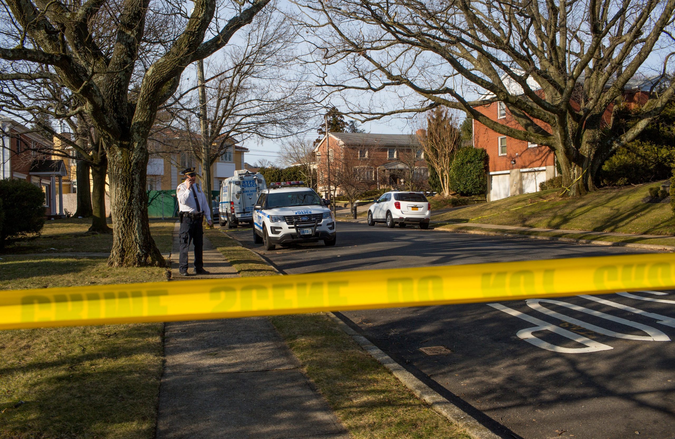 Yellow police tape is seen on a tree-lined city block with large homes.