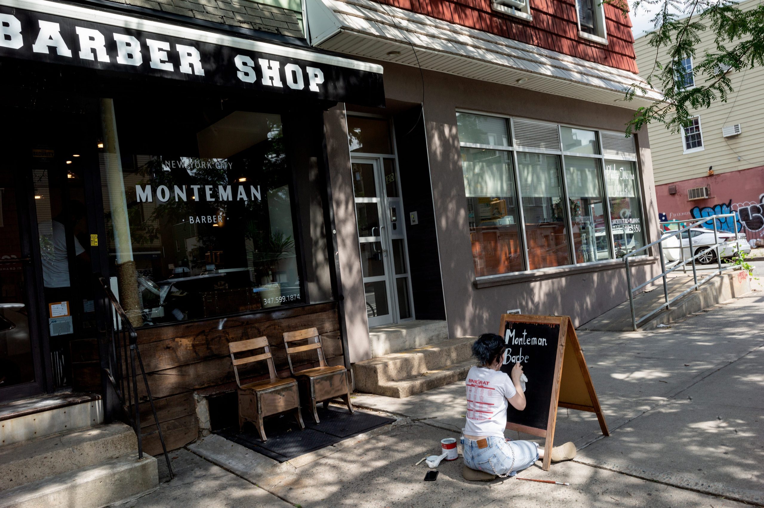 A person writes on a small black chalkboard outside a barbershop.