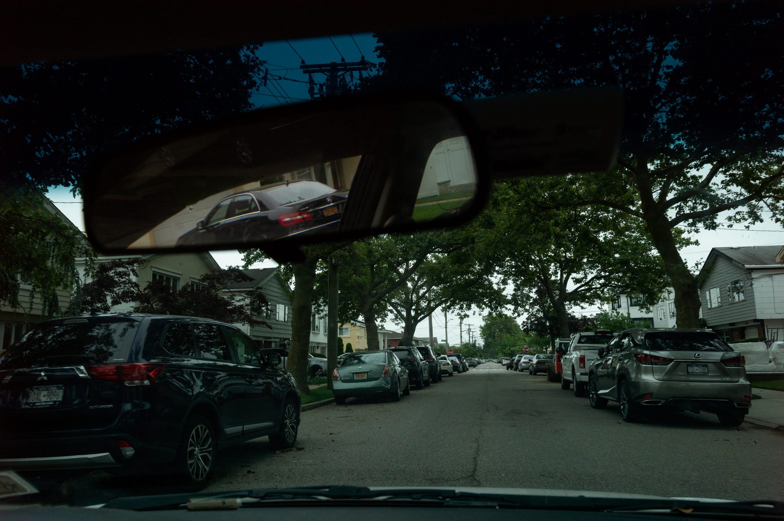 A tree-lined street is seen through the front window of a car.