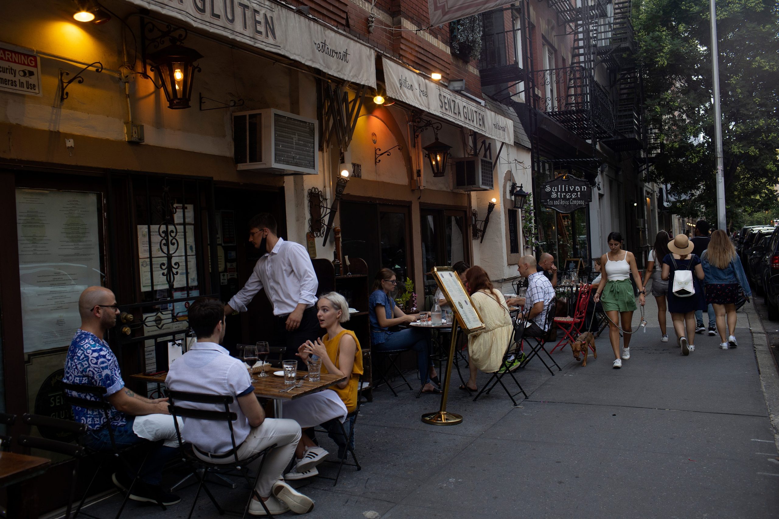 People seated at sidewalk tables outside a restaurant.