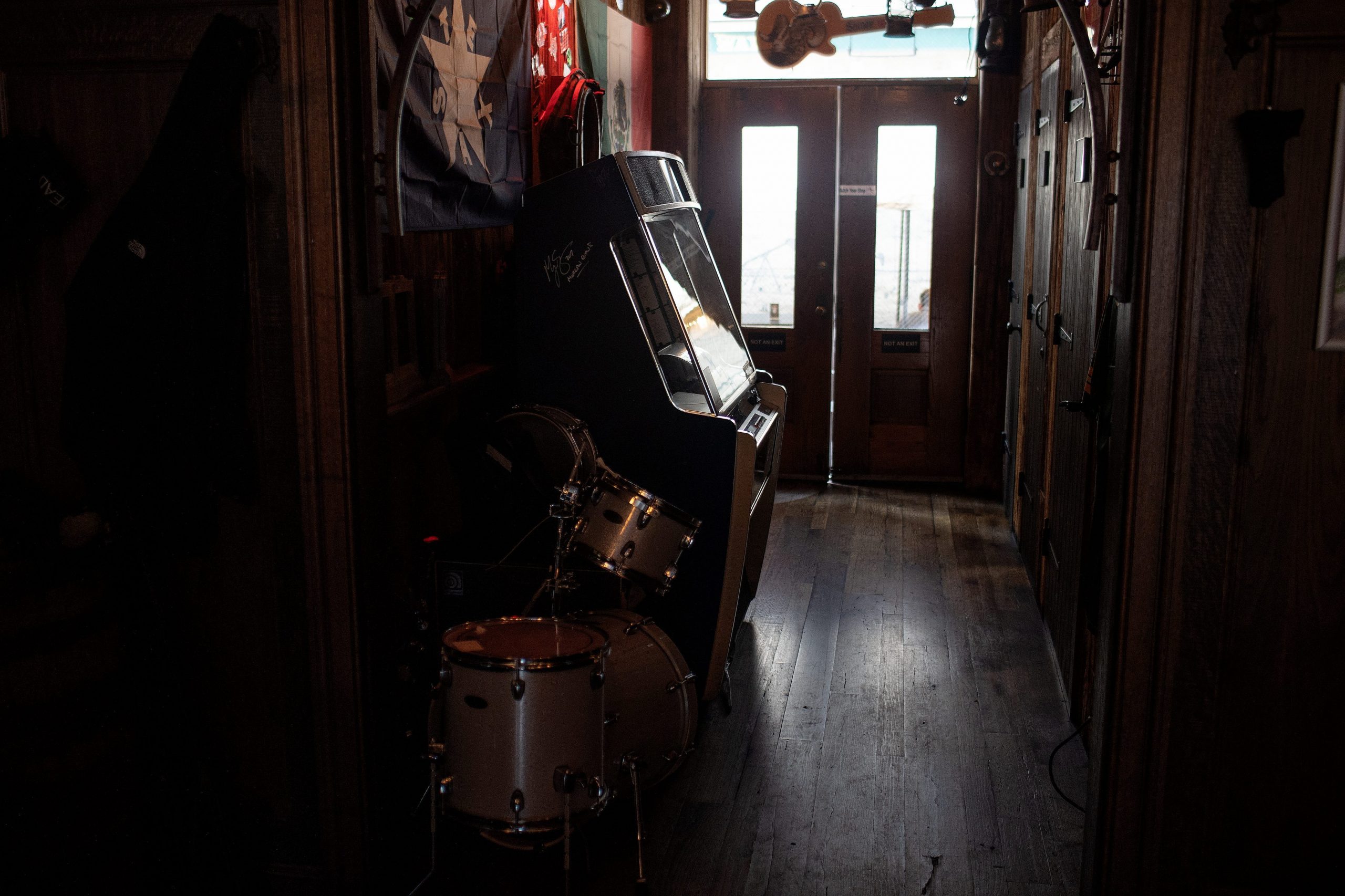 Looking toward a door, from which the sun pours through, a jukebox is seen in the foreground.